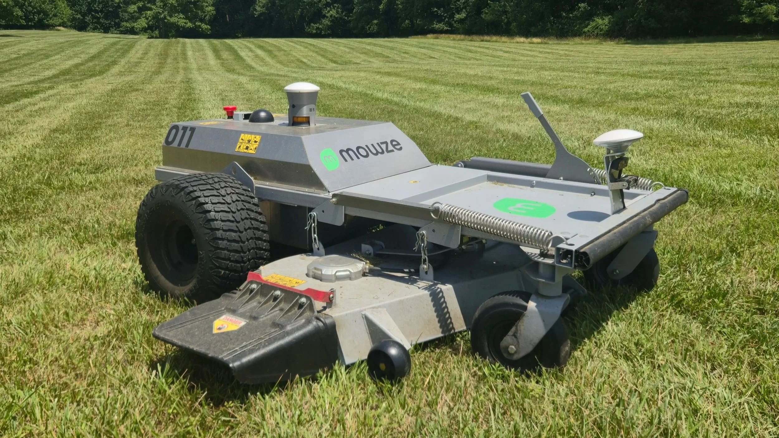 The MOWZE M60 all electric robotic mower on a grassy field, with trees in the background.