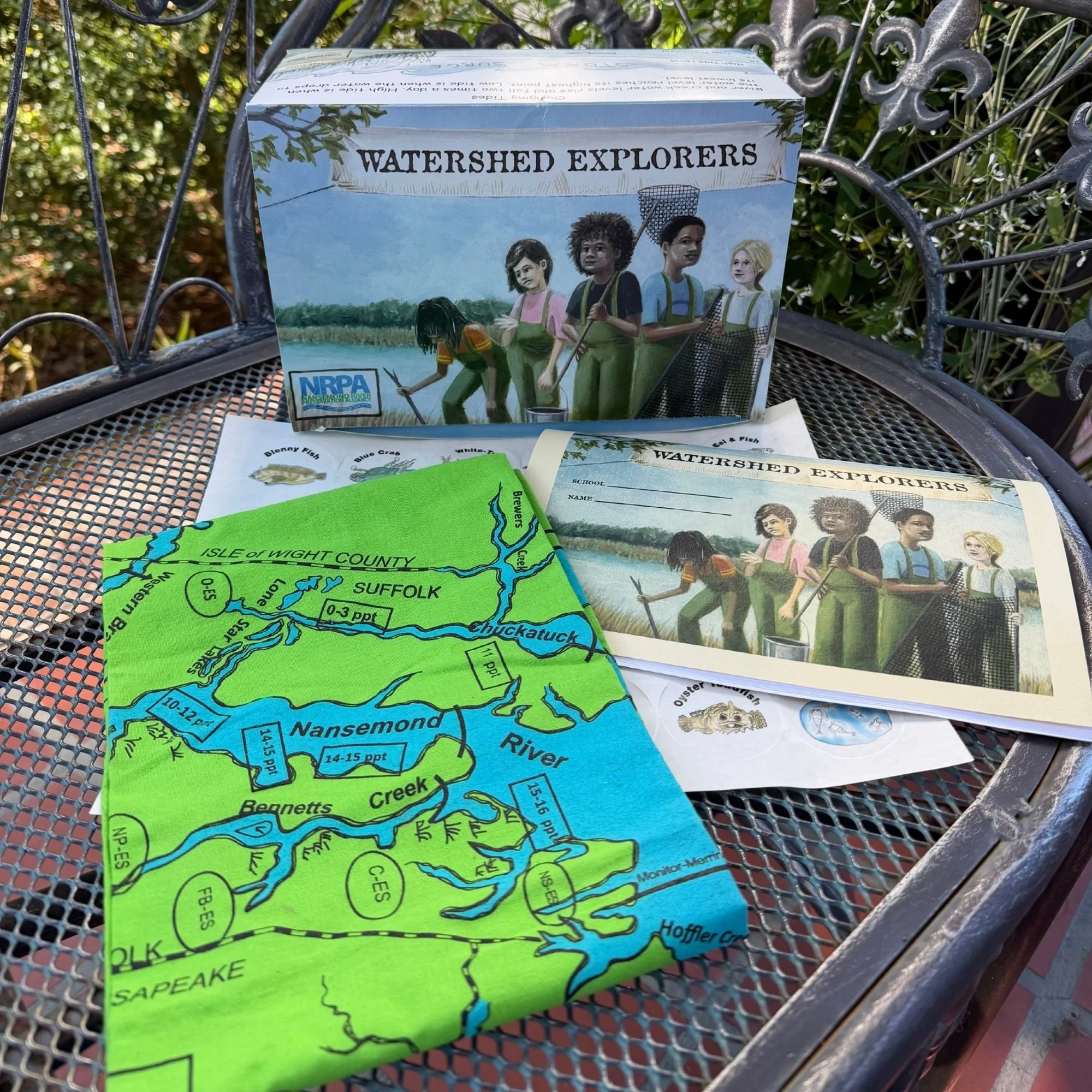A box titled 'Watershed Explorers' leaning against a metal bench outdoors, with a map of the Connecticut River Watershed and informational pamphlets nearby.