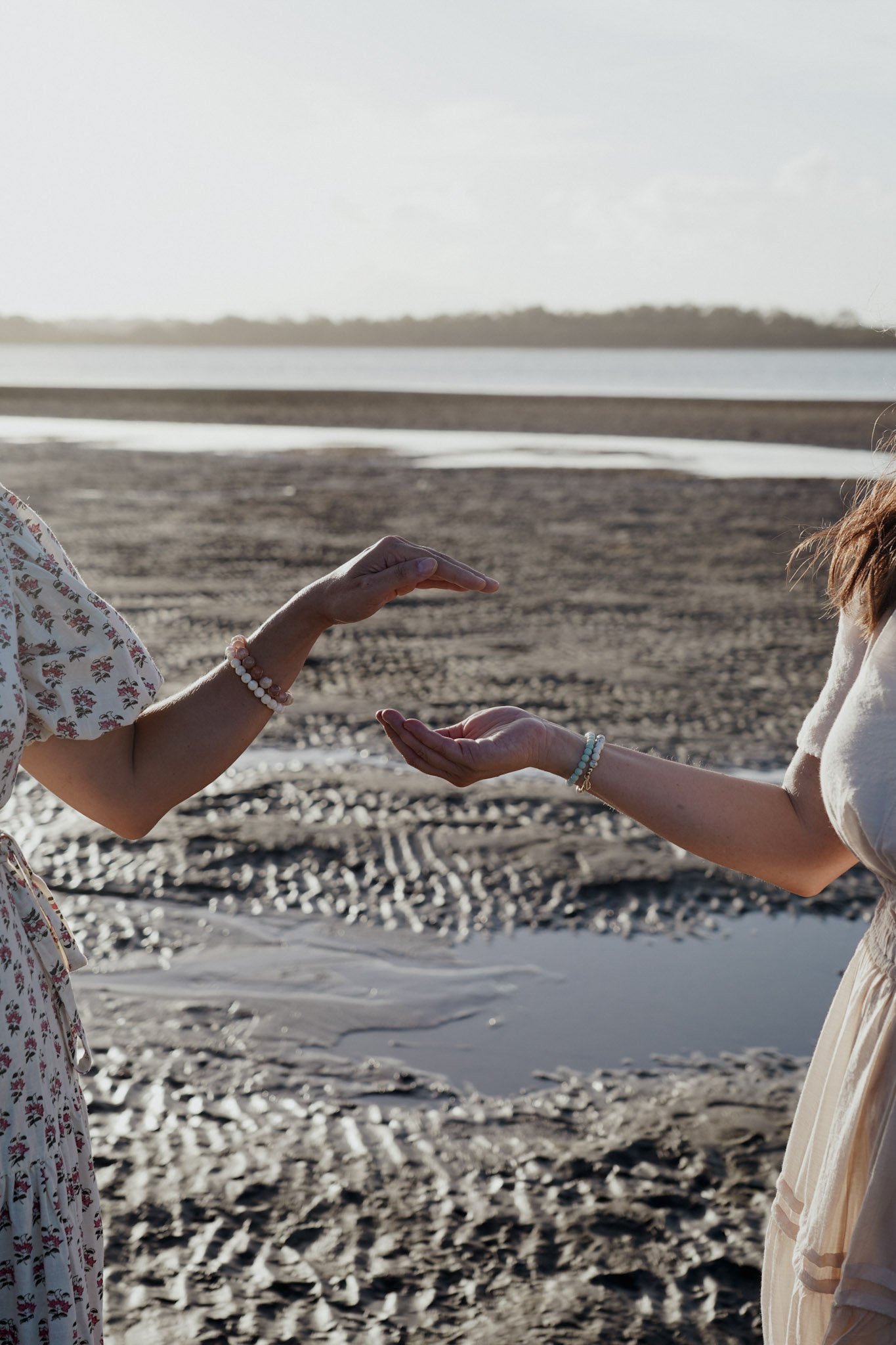 Two women exchanging reiki energy on the beach during sunset, with water in the background.