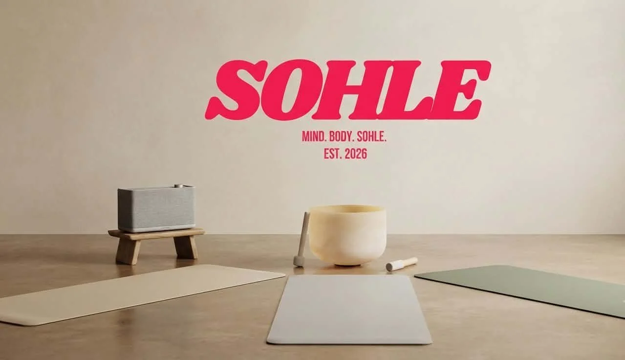 Yoga mats, a singing bowl, and a speaker on a wooden floor in front of a wall with SOHLE logo in pink and the words 'Mind, Body, Sohle. Est. 2026'.