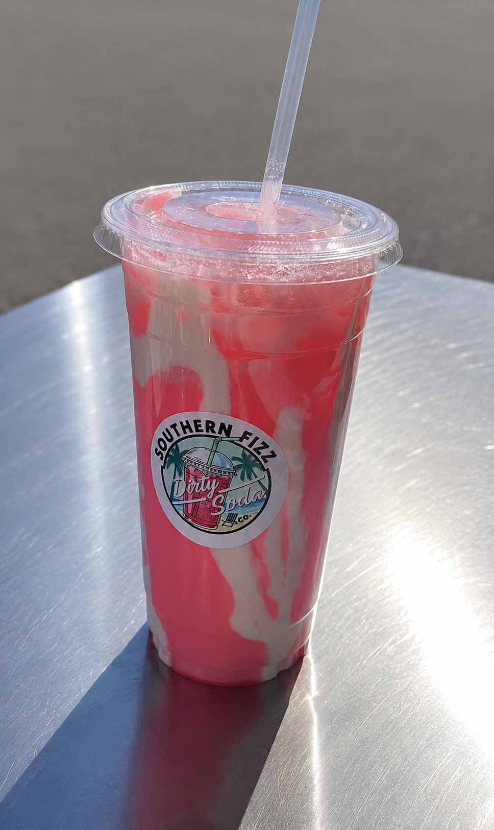 A plastic cup filled with pink and white swirl soda with a straw on a shiny metallic surface.