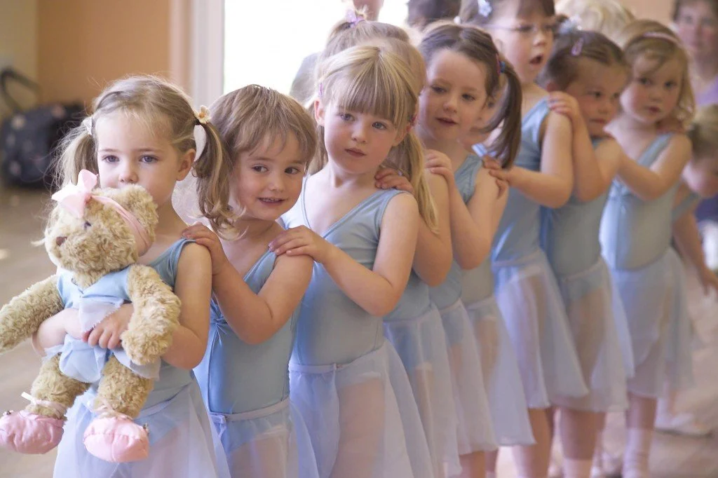 Line of young girls in matching ballet costumes waiting in a dance studio.