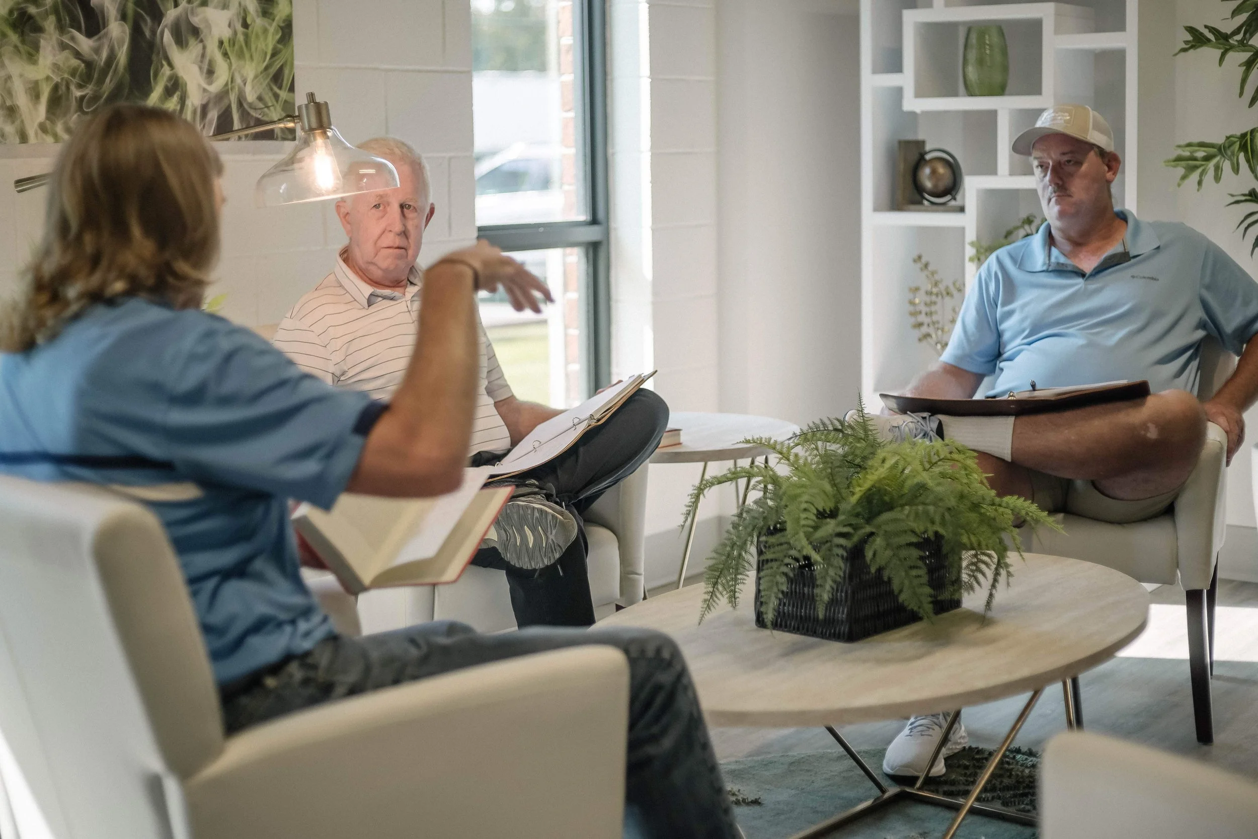 People sitting in a room having a discussion, with a potted plant on a table in the foreground.