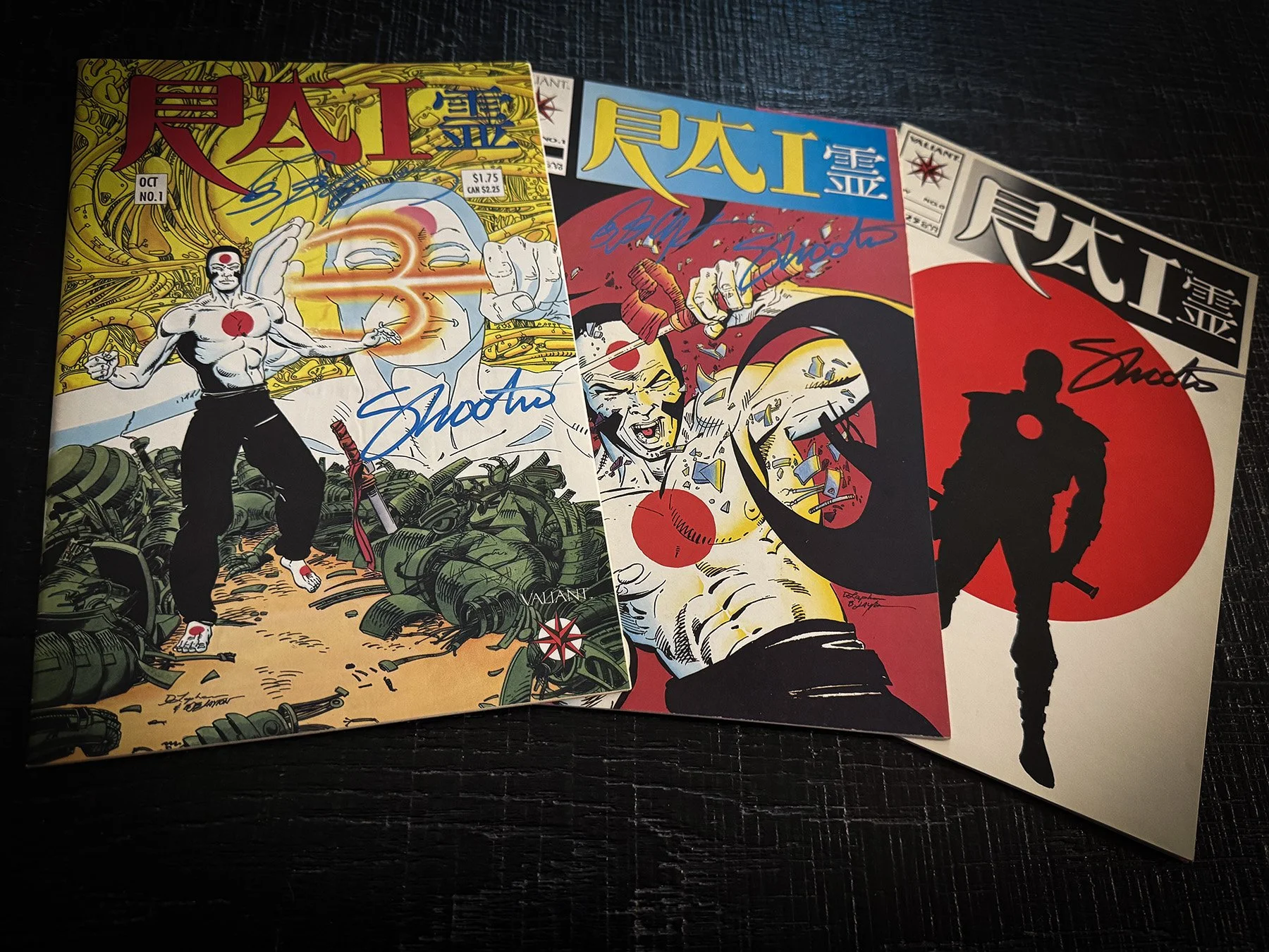 Three signed Valiant Rai comic books displayed on a dark tabletop. The group includes the Magnus Robot Fighter #5/Rai flipbook, Rai #1 and Rai #0, each autographed by Jim Shooter in blue or black ink.