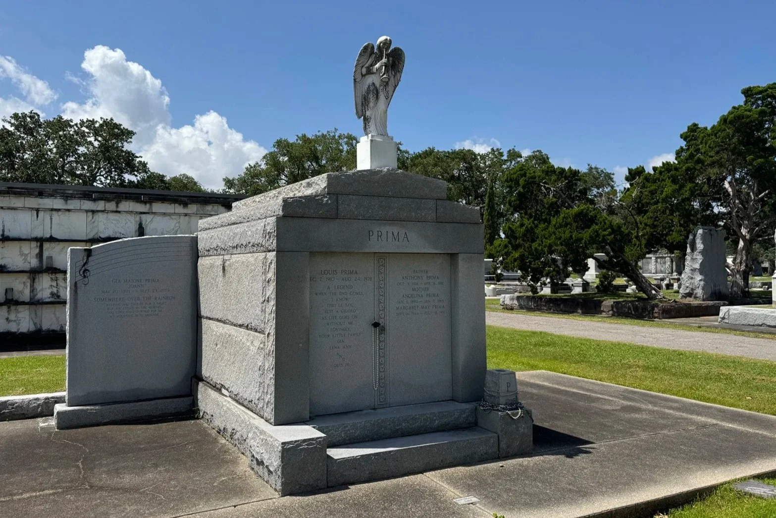 Gray granite Louis Prima family tomb topped by an angel statue in Metairie Cemetery.