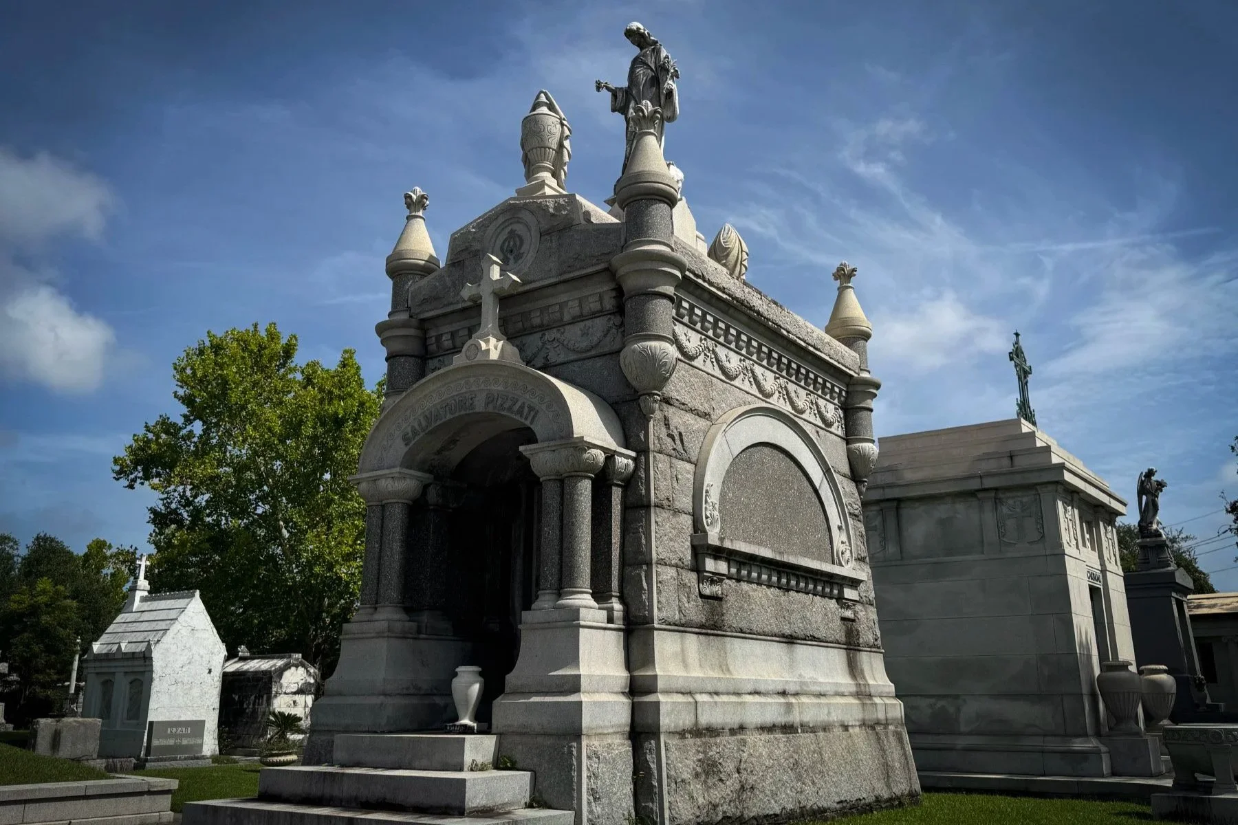 Ornate stone Salvatore Pizzati Mausoleum beneath a blue sky in Metairie Cemetery, New Orleans.