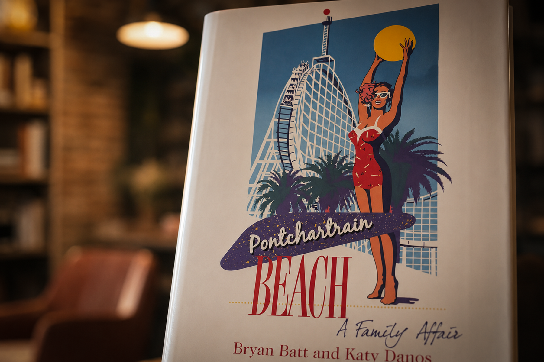 Pontchartrain Beach: A Family Affair by Bryan Batt and Katy Danos displayed on a stand inside a softly lit independent bookstore, with the book cover in sharp focus against a blurred background of bookshelves and warm natural light.