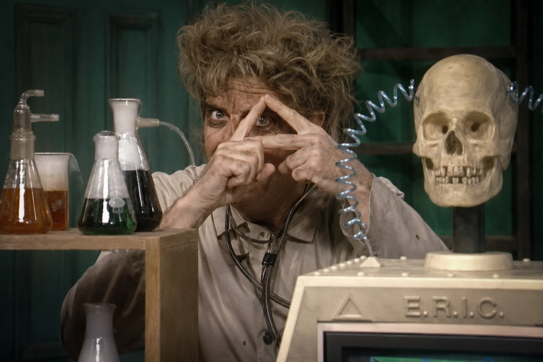 Morgus gestures beside laboratory glassware and E.R.I.C., a talking skull connected to an Apple II computer, during the 1987 television revival.