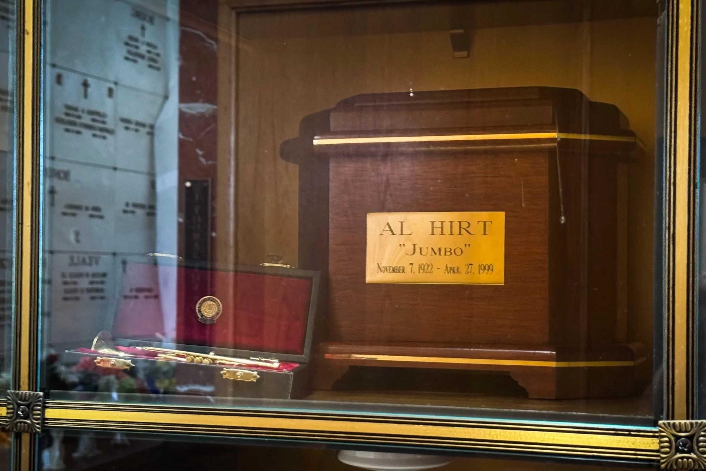Al Hirt’s wooden urn displayed beside a miniature trumpet-shaped award in a glass-fronted niche at the All Saints Mausoleum.