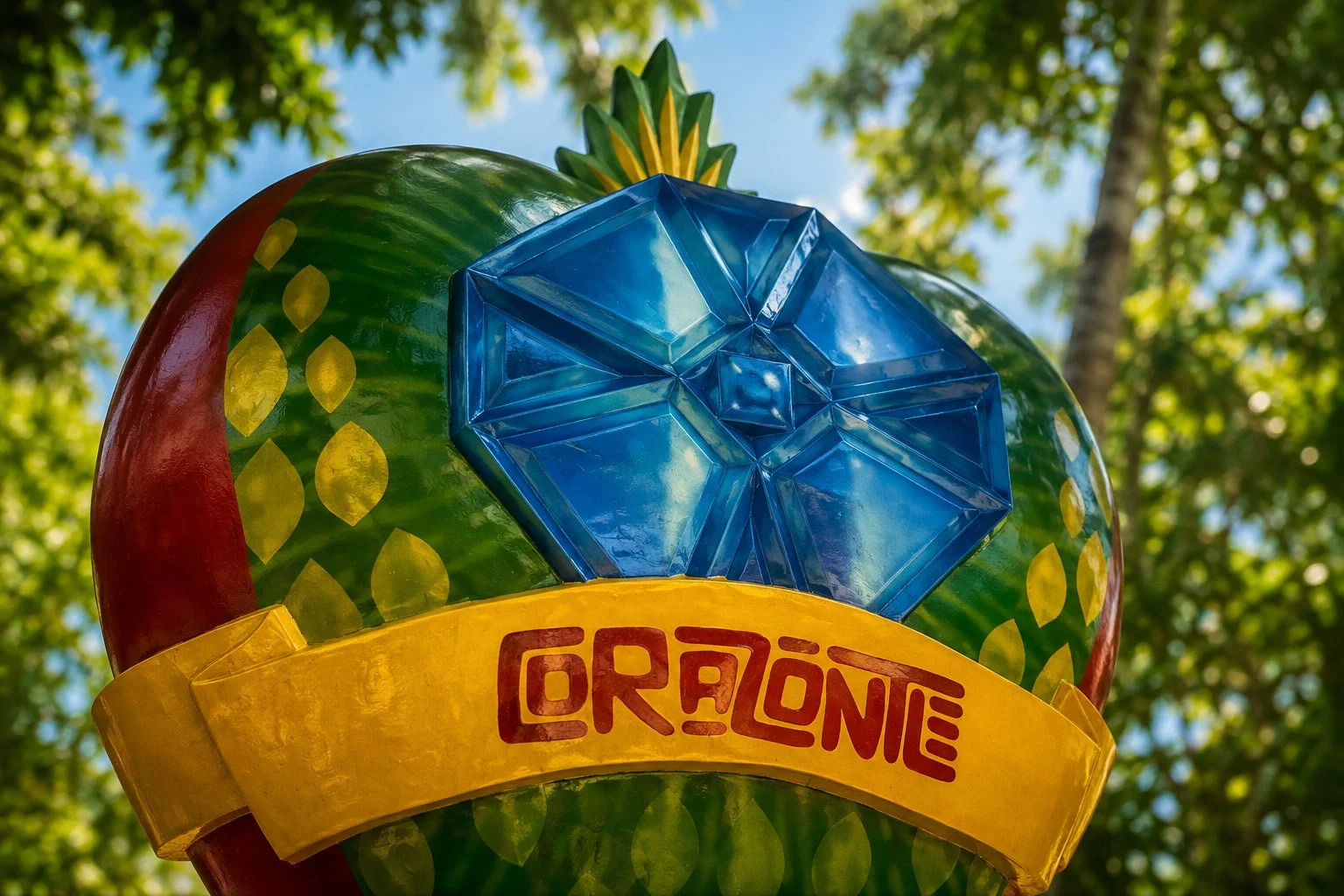 Colorful Corazontle entrance sign featuring a blue luchador mask against a green globe, photographed from below beneath tropical trees.