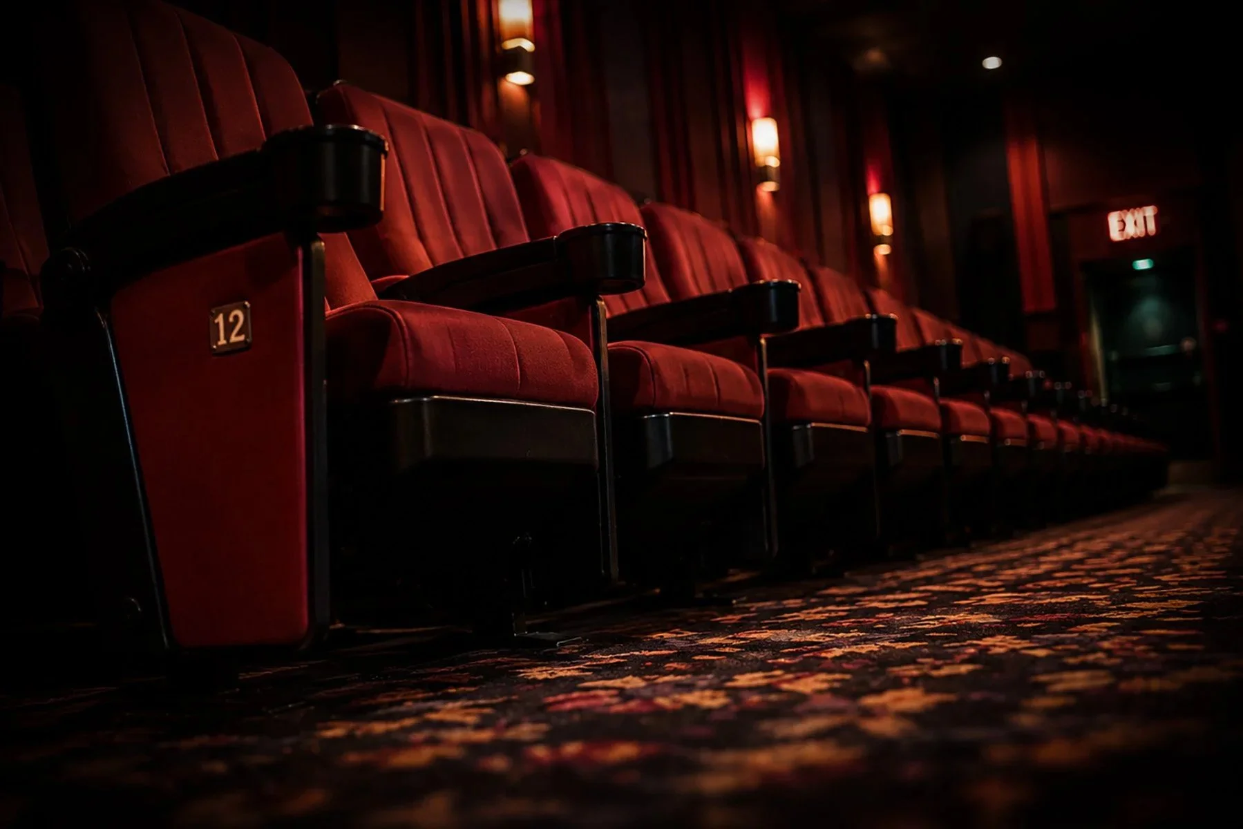 Rows of empty red theater seats inside a dark movie auditorium, illuminated by warm aisle lights as they await the start of the next film.