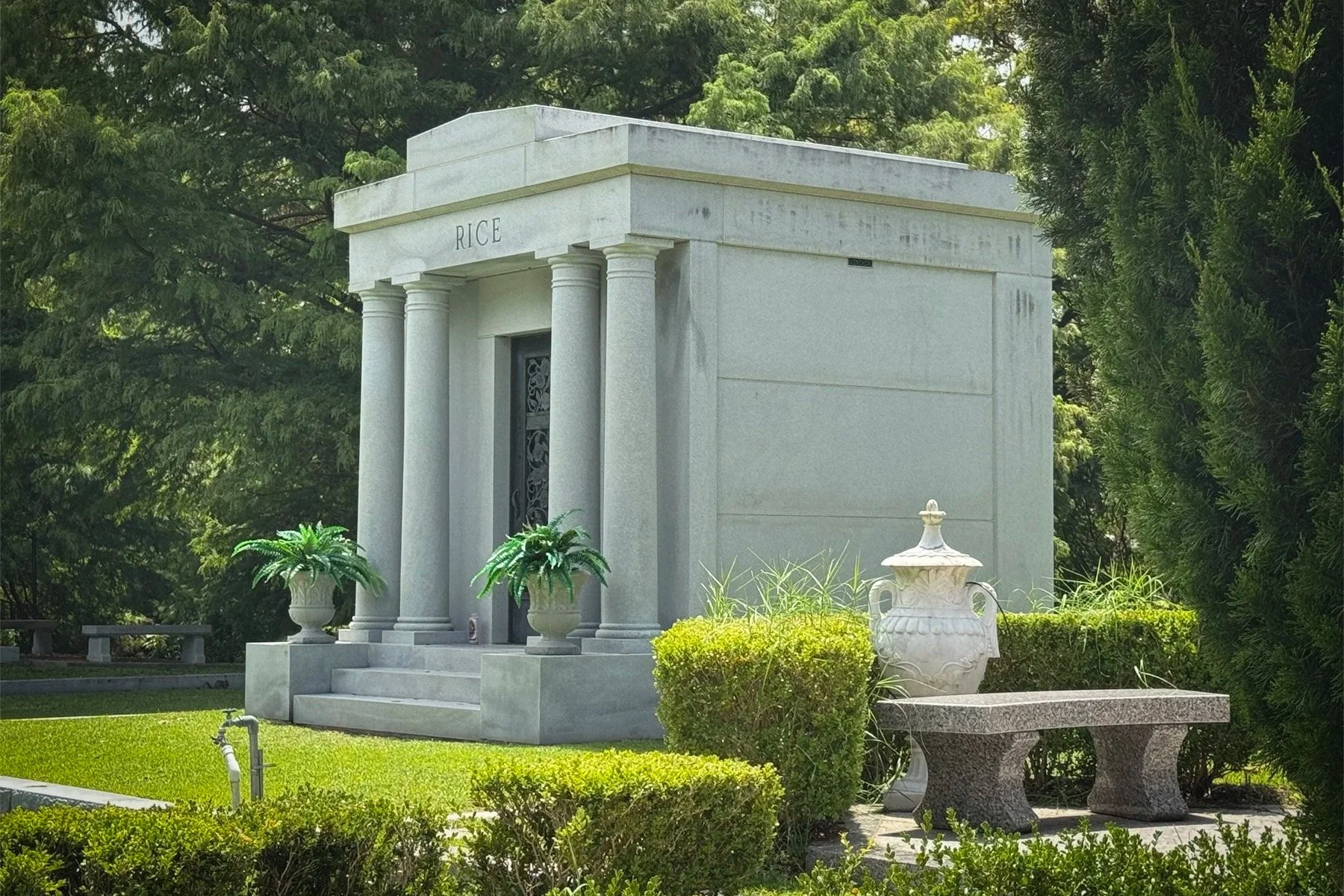 Gray stone Rice family tomb with four columns and landscaped grounds in Metairie Cemetery.