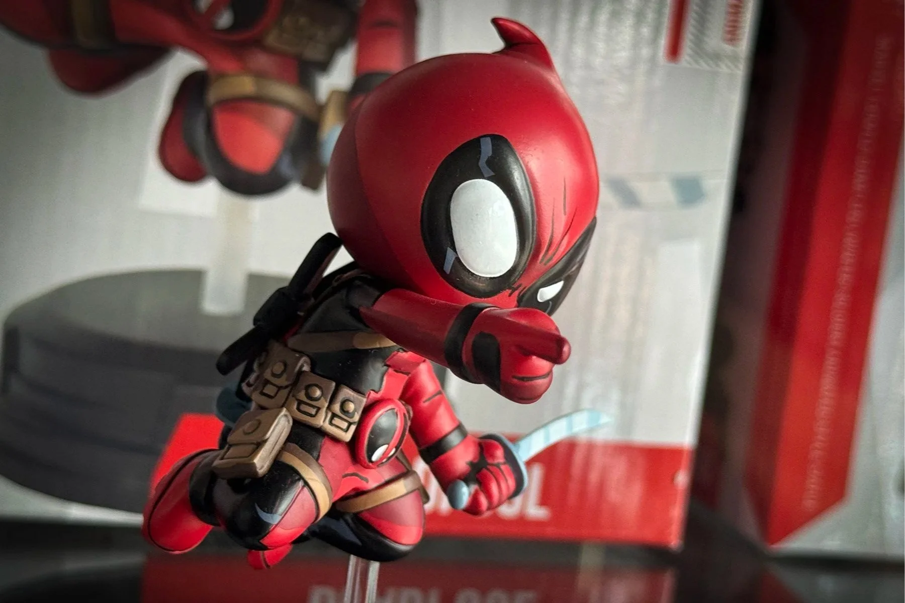Red Deadpool figure displayed in its packaging inside a comic shop.