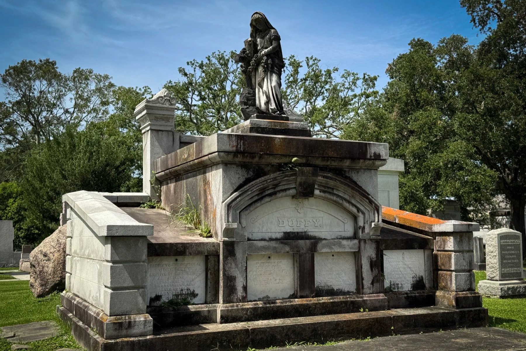 Weathered Duffy family tomb topped by a mourning statue in Metairie Cemetery, New Orleans.