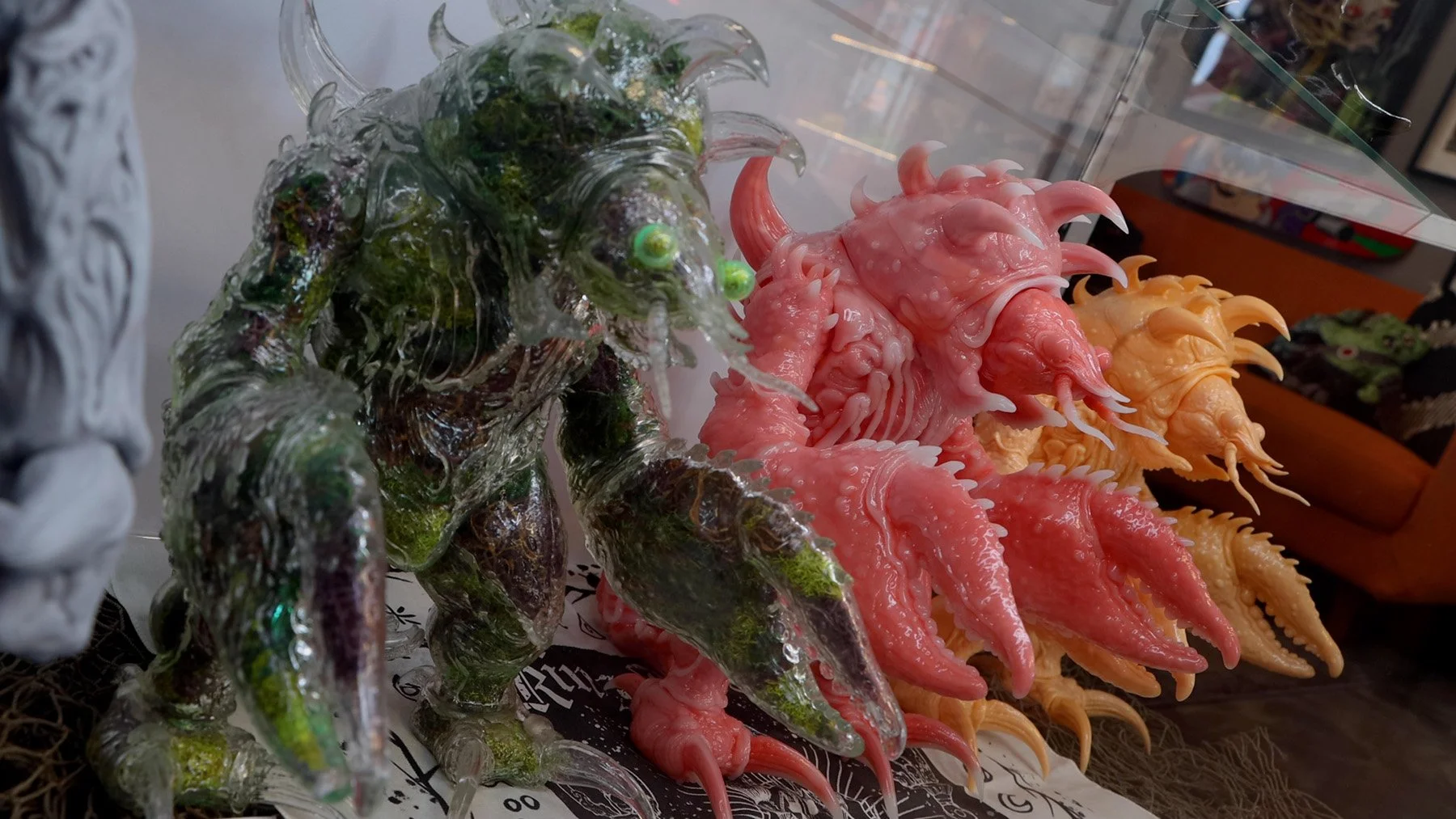 Green, pink and yellow King Krawju designer figures with crawfish claws, horns and textured monster bodies inside a glass case.