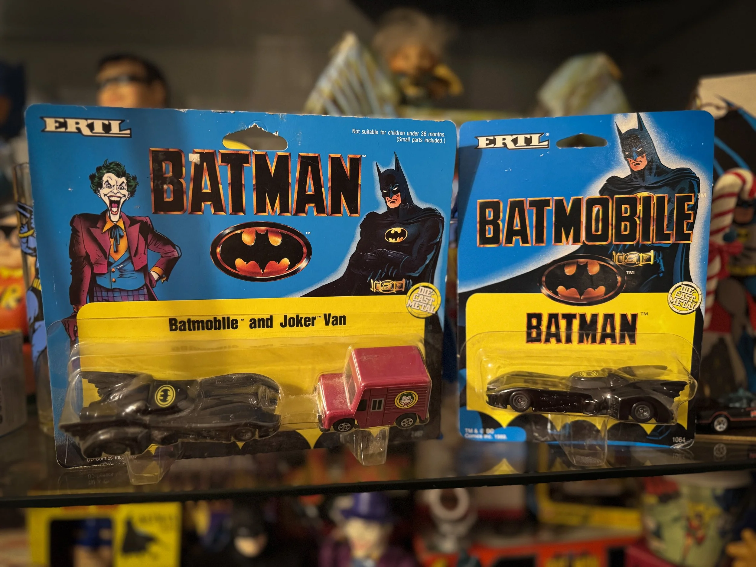 Two unopened ERTL Batman (1989) die-cast vehicle packages featuring the Batmobile and Joker Van displayed on a collector's shelf.