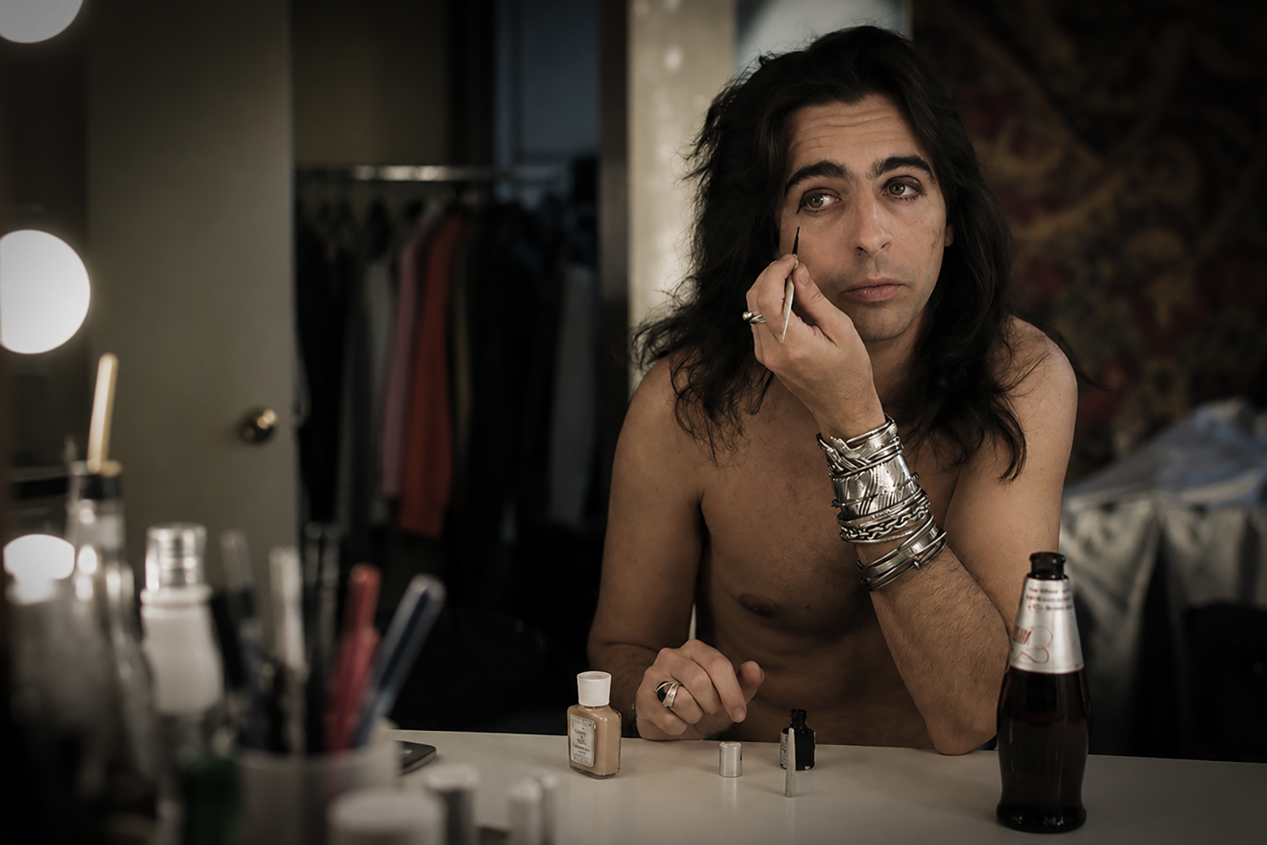Young Vincent Furnier applying Alice Cooper’s signature black eye makeup at a dressing-room mirror.
