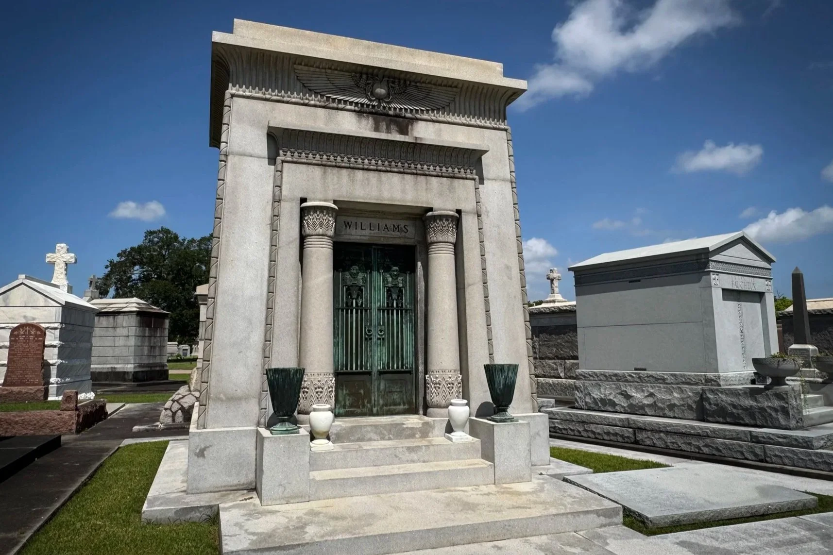 Egyptian Revival Williams family tomb with carved winged sun disk, papyrus columns and bronze doors in Metairie Cemetery.