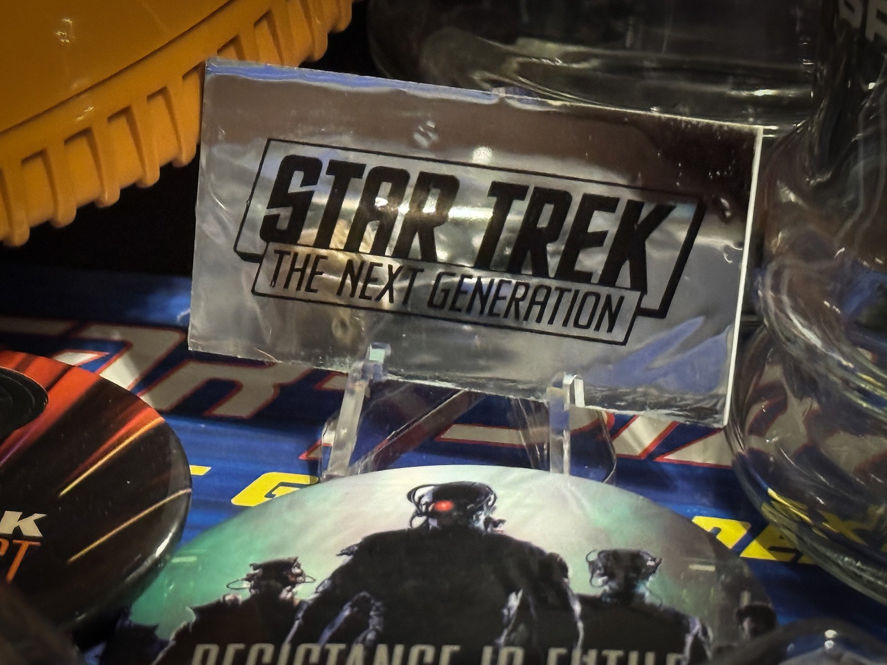 Vintage holographic Star Trek: The Next Generation promotional pin displayed on a small stand among Star Trek memorabilia.