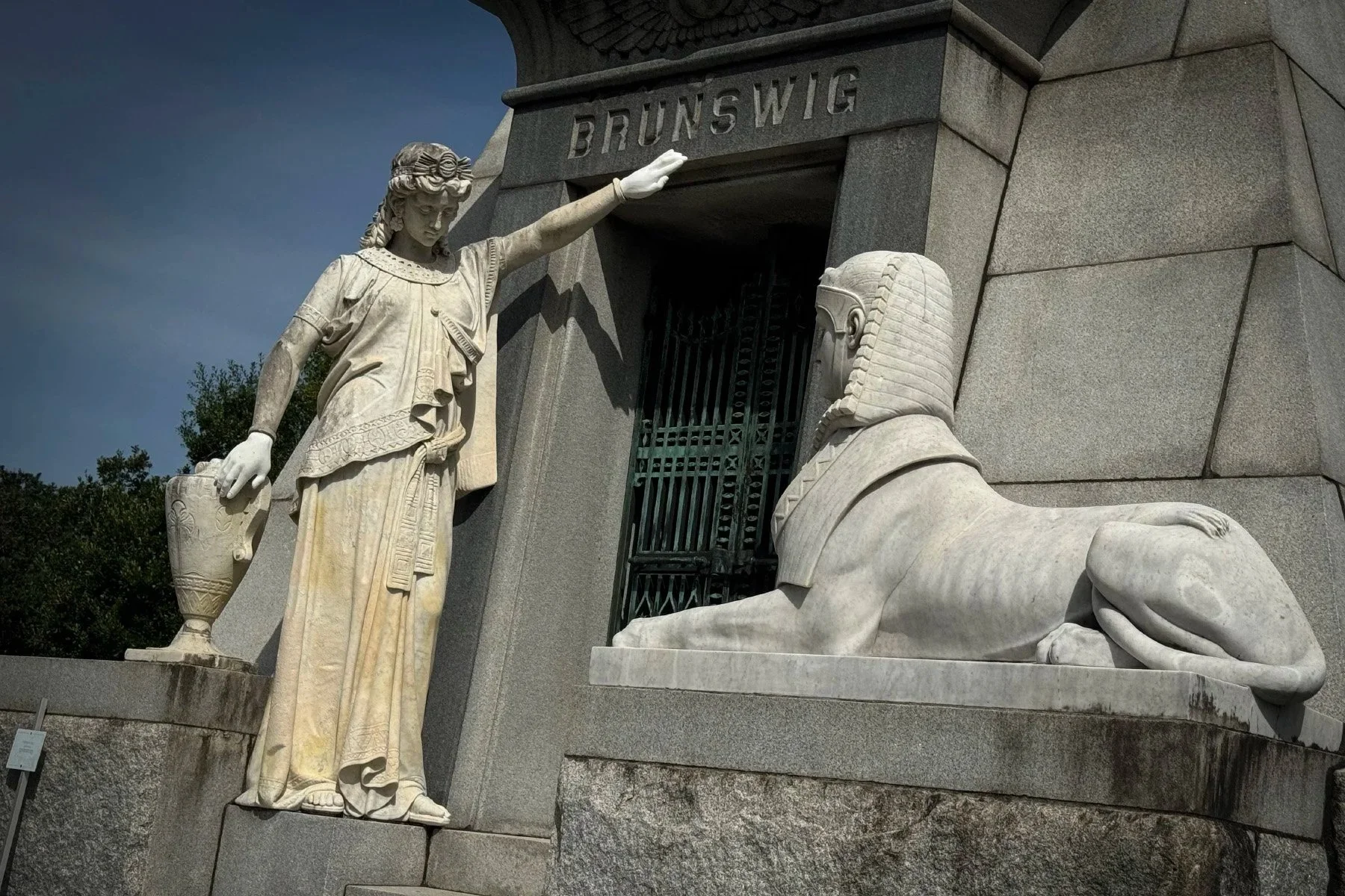 Sphinx and seated female figure holding an urn outside the pyramid tomb of Lucien Brunswig in Metairie Cemetery, New Orleans.