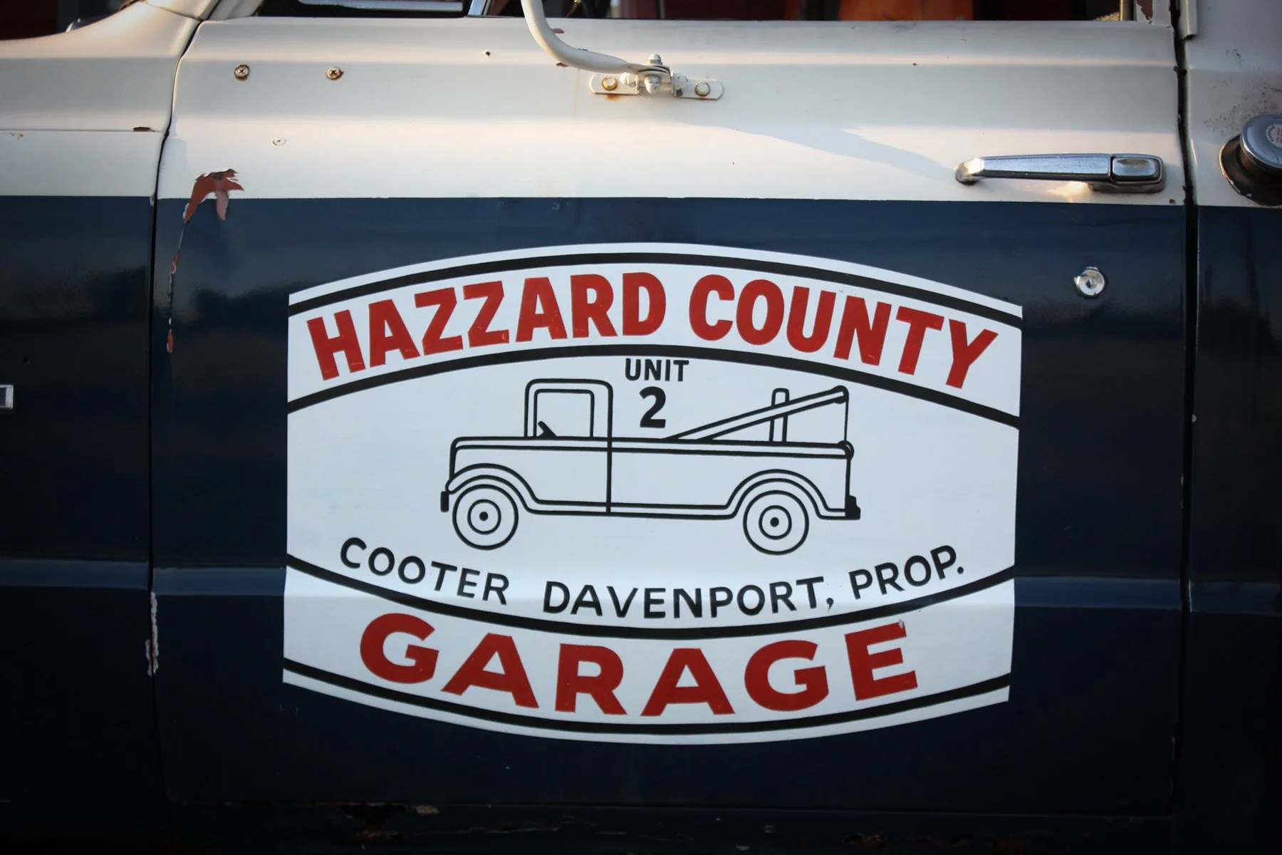Weathered tow truck door marked “Hazzard County Unit 2, Cooter Davenport, Prop., Garage.”