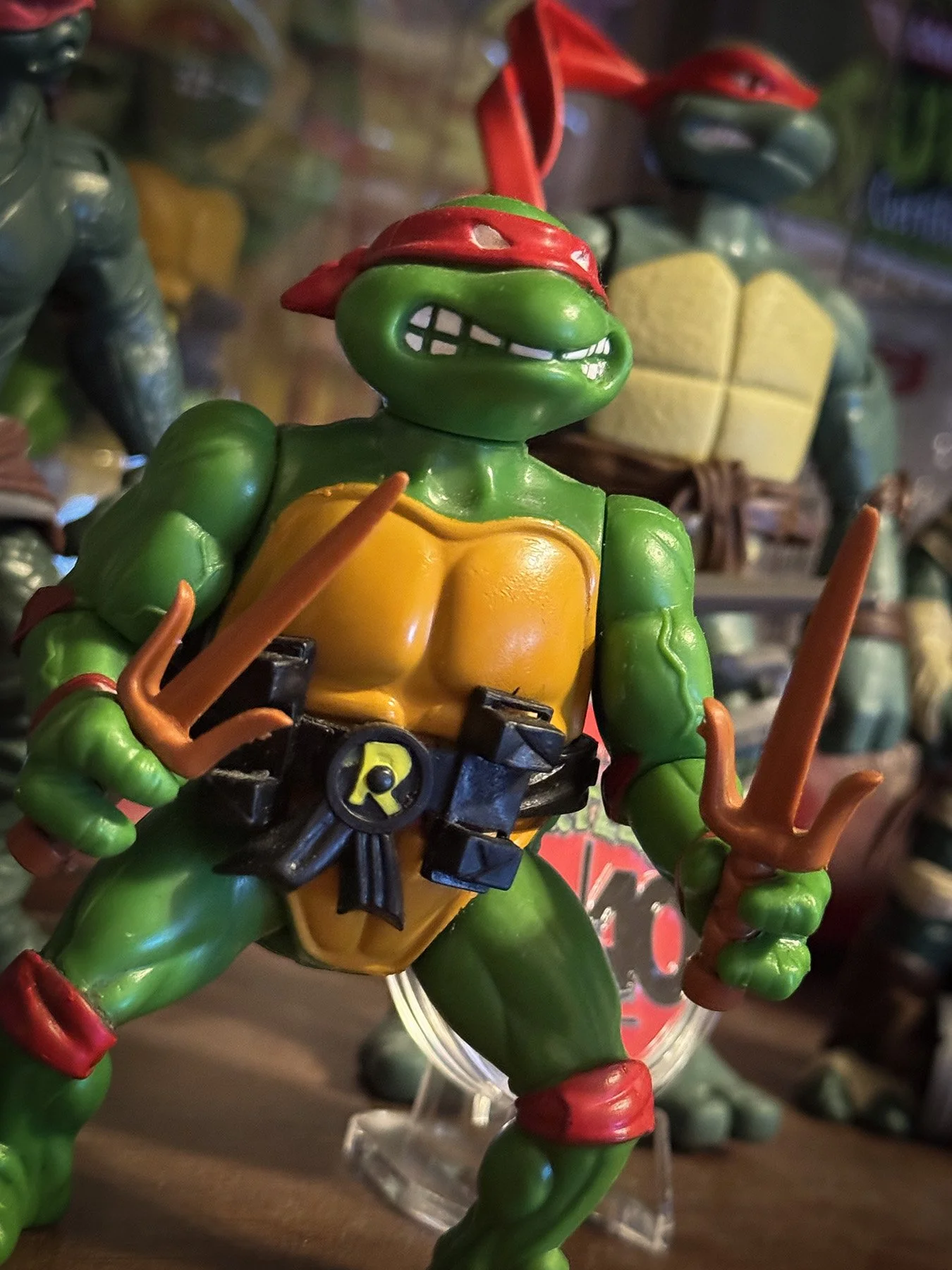 Vintage Playmates Raphael action figure from Teenage Mutant Ninja Turtles posed with twin sai in front of additional turtle figures, highlighting one of the defining toy lines of the late 1980s and early 1990s.