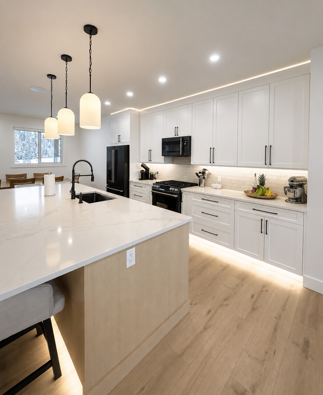 Modern kitchen with white cabinets, black appliances, and a large island with a marble countertop, pendant lighting, and a window with snowy scenery outside.