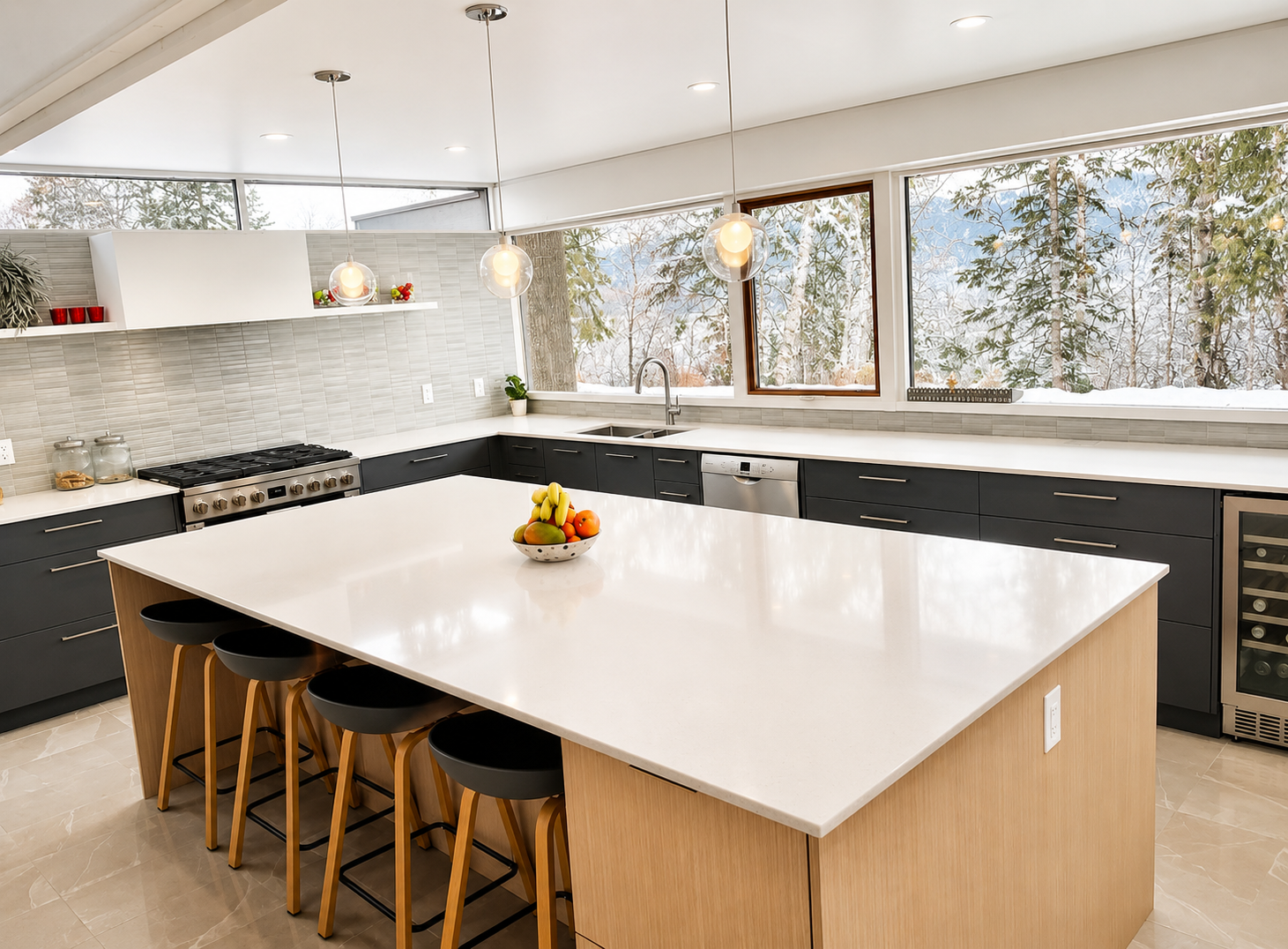 Modern kitchen with large white island counter, black cabinets, stainless steel appliances, three hanging pendant lights, and large windows showing snow-covered trees outside.