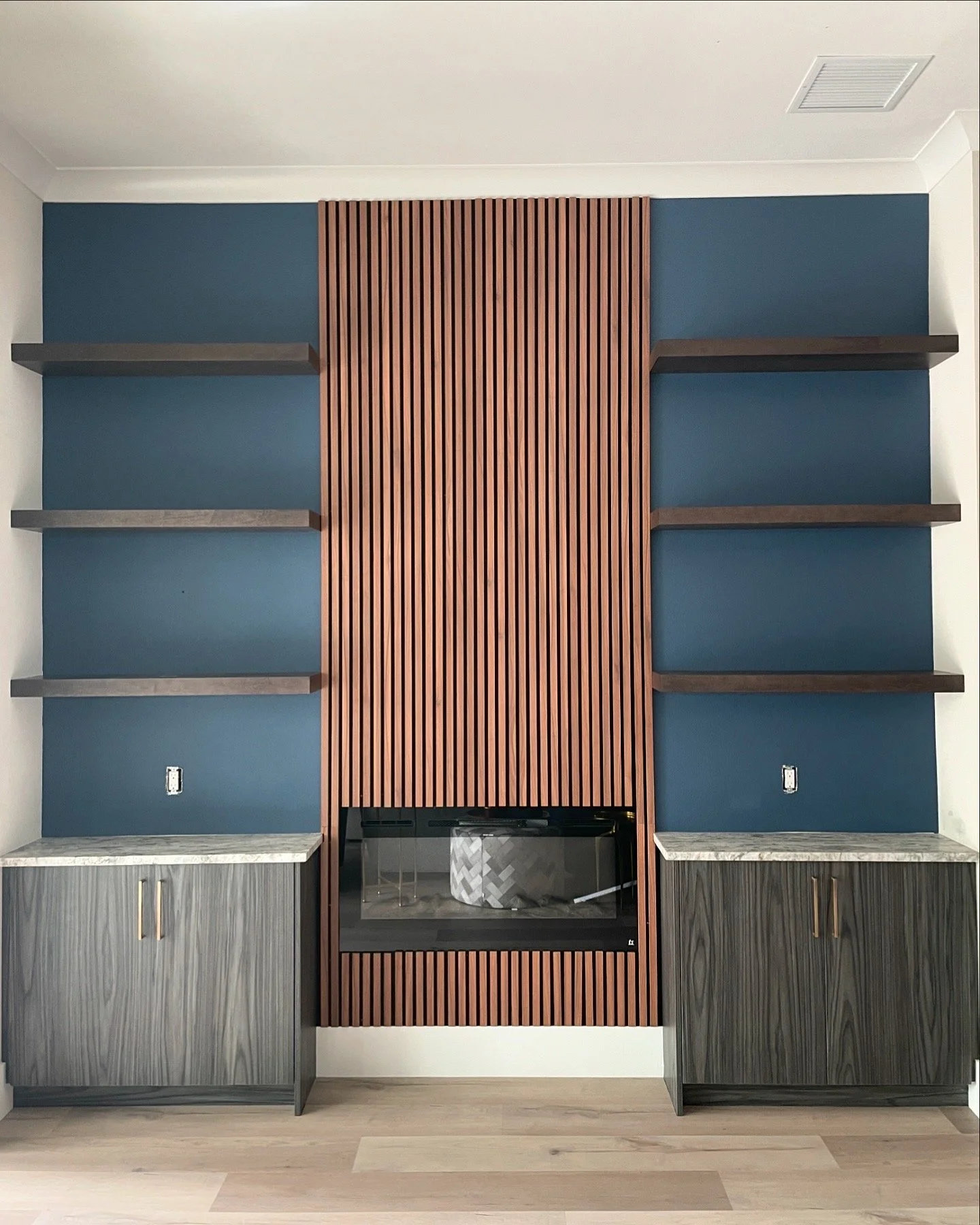 Modern living room wall with built-in fireplace, blue wall panels, and open wooden shelves above a marble top cabinetry.