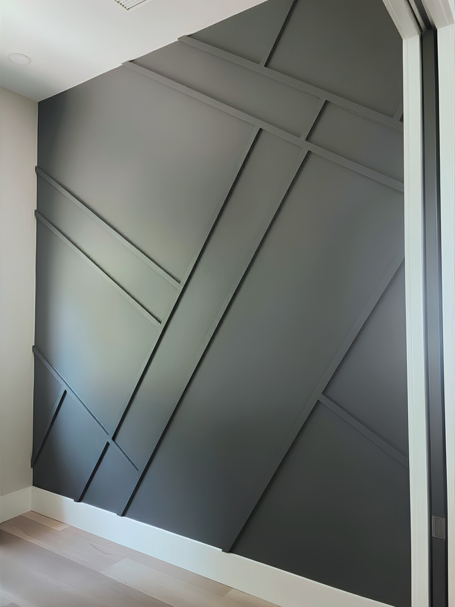 Interior view of a room with a ceiling that has sloped, dark-colored panels and white support beams, next to a sliding glass door.