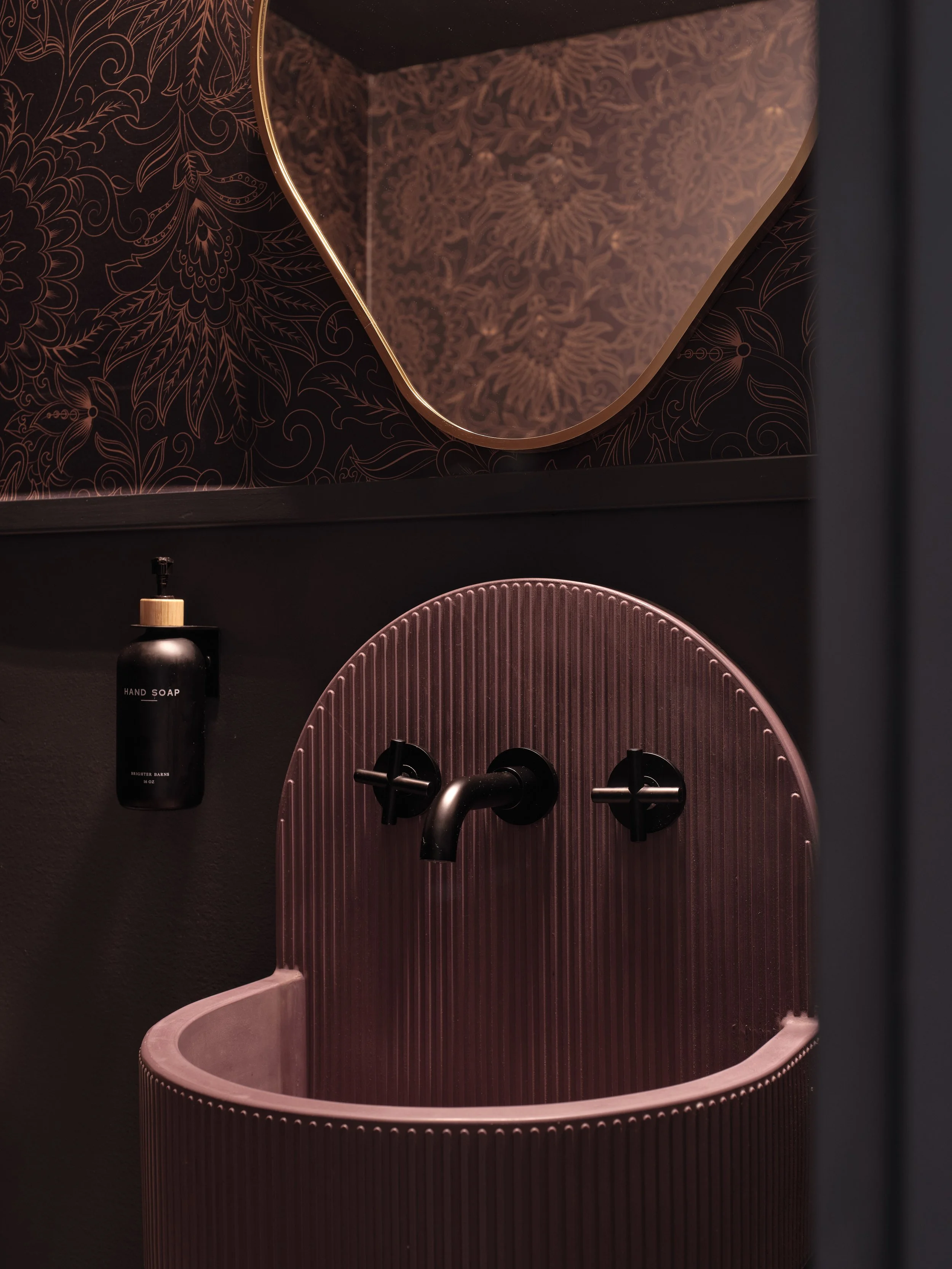 A pink sink with black faucet and handles, a black hand soap bottle labeled 