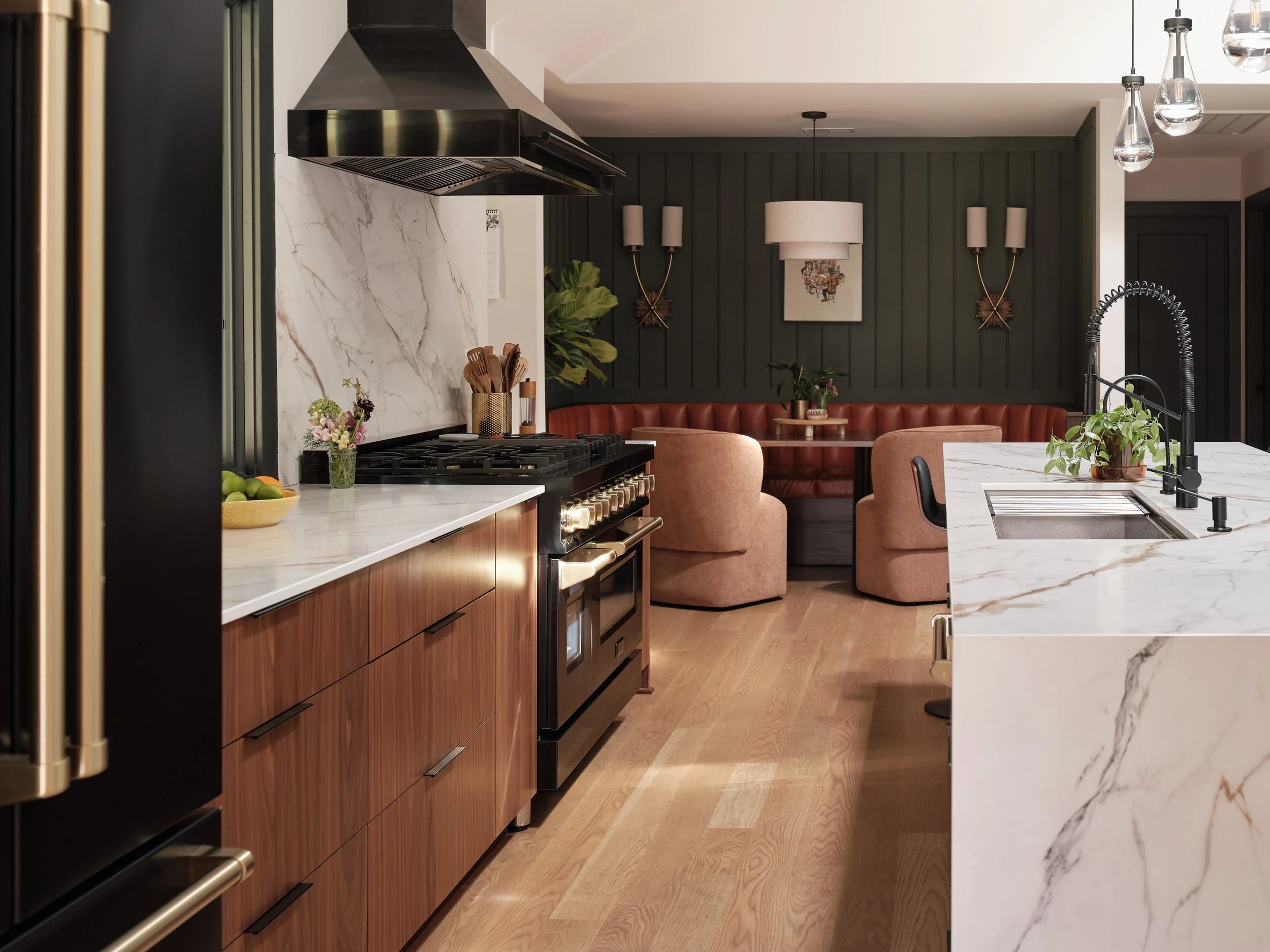 Modern kitchen featuring a black stove with a range hood, wooden cabinets, a marble countertop with a bowl of fruit, and a marble island with a black faucet.