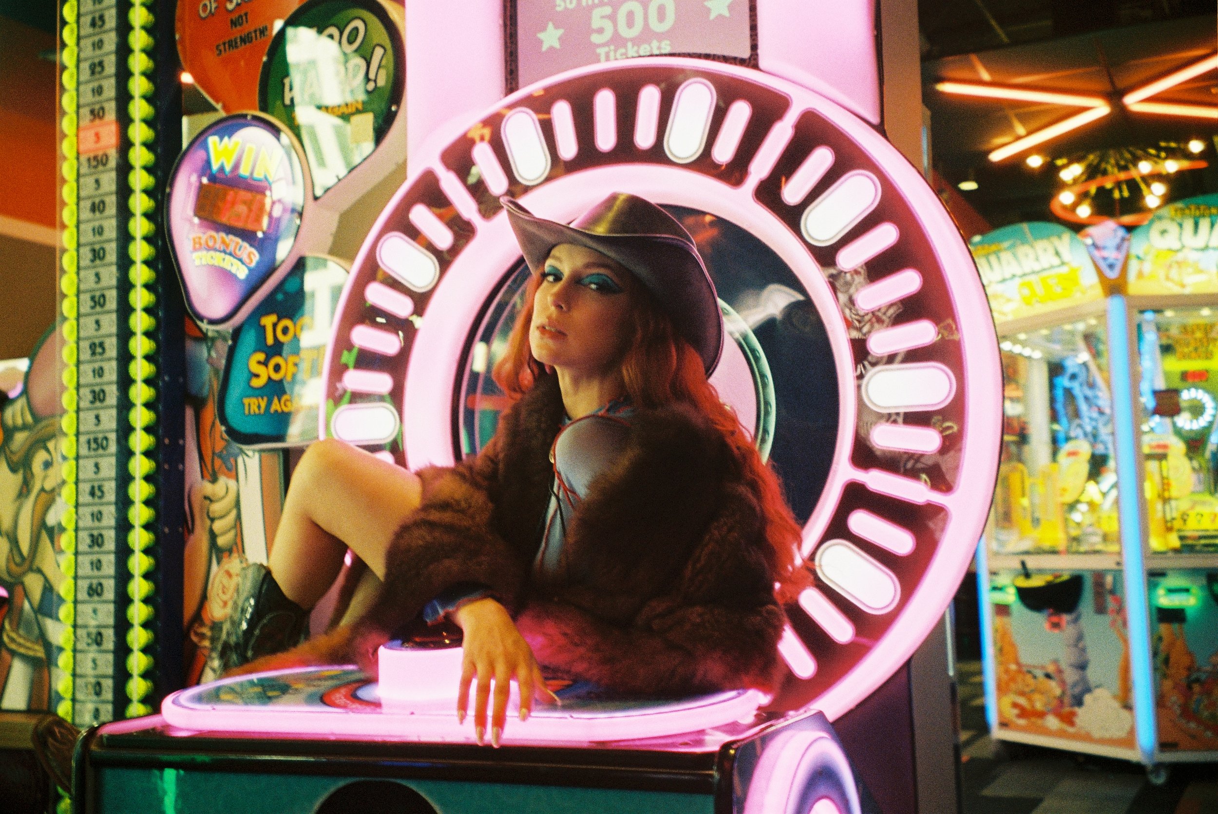 Artist press photo on film: cowboy hat, fur coat, sitting on an arcade machine, by Stephanie Cousino
