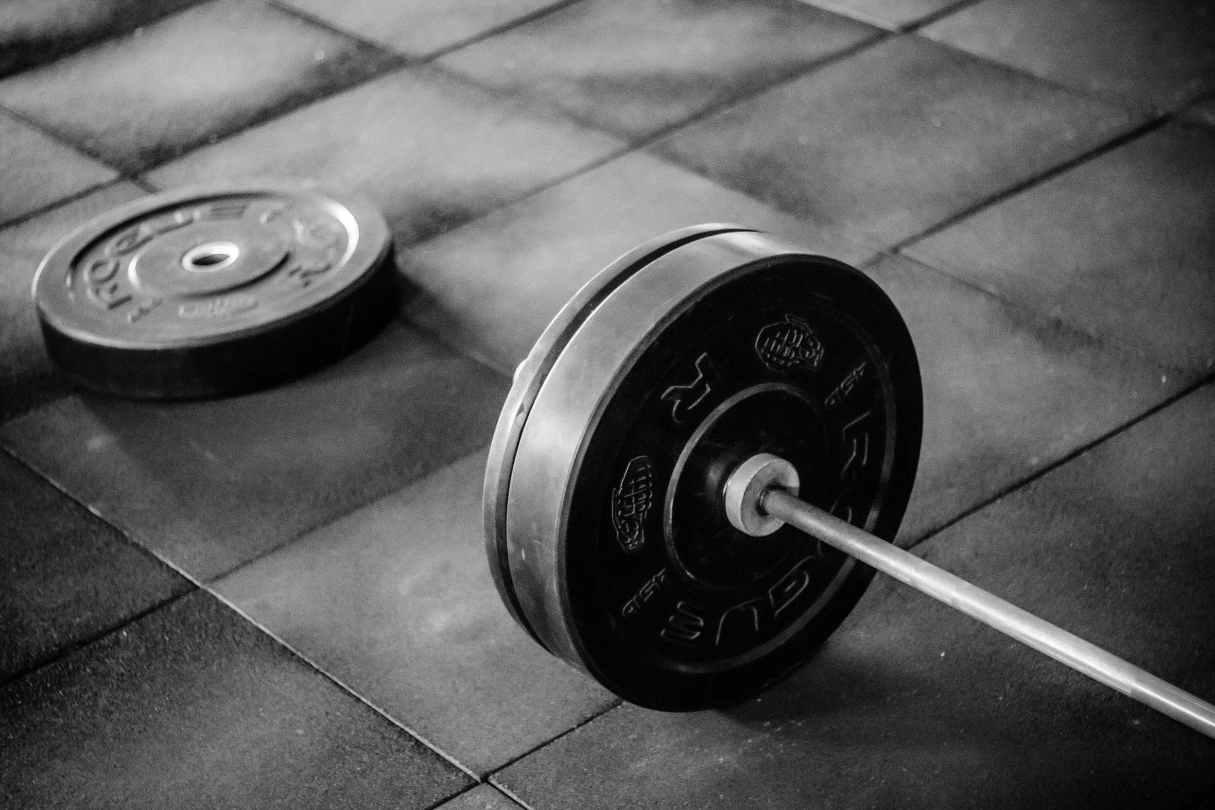 Black and white photo of a pair of dumbbells resting on a wooden surface.