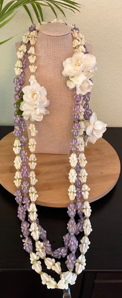 A floral lei with white and purple flowers draped over a beige necklace display bust on a wooden surface.