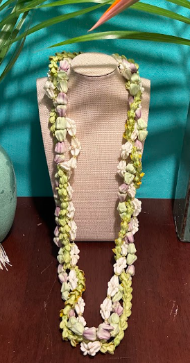 A beige tote bag with a floral lei draped over it, placed on a beige stand against a teal background with some green and pink decorative elements.