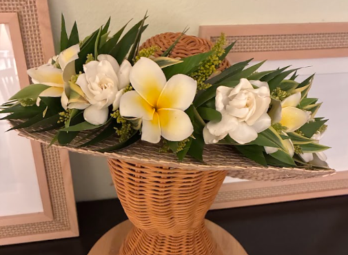 A flower arrangement with white roses and yellow and white plumeria in a woven wicker basket