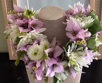 A floral necklace with pink, white, and green flowers displayed on a beige bust stand.