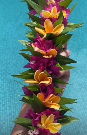A floral lei made of yellow and purple flowers with green leaves.