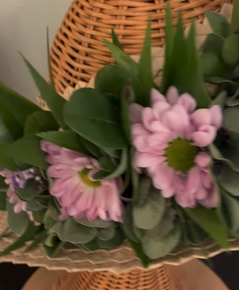 Close-up of pink daisy flowers with green centers and green foliage in a wicker basket.