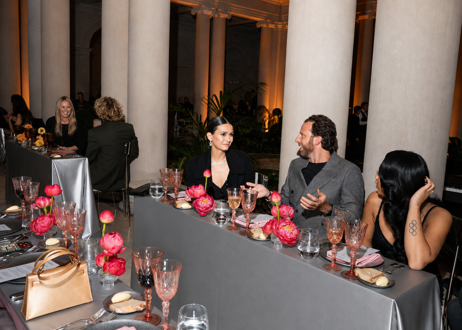People seated at a banquet table engaged in conversation at a formal event with elegant decor and pink flower centerpieces.