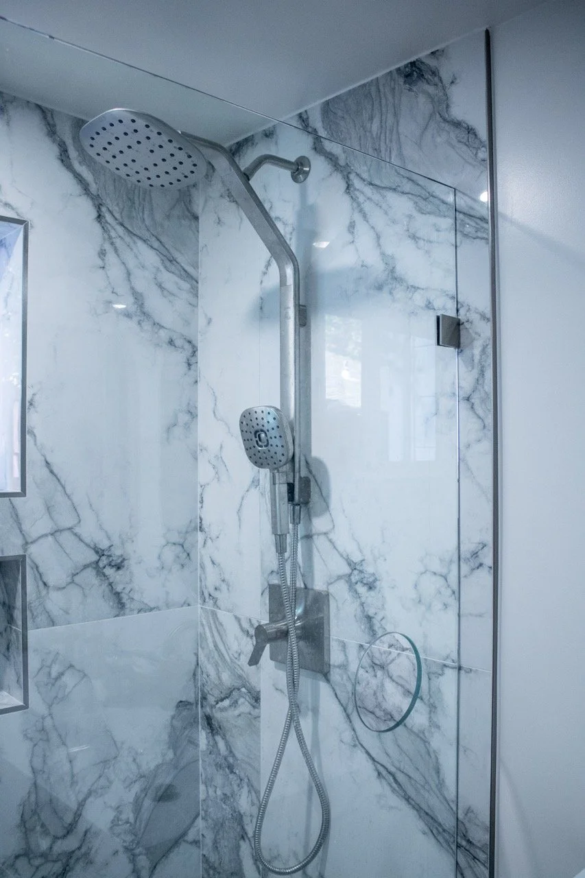 Shower with marble tile walls, rainfall showerhead, and handheld showerhead in a modern bathroom.