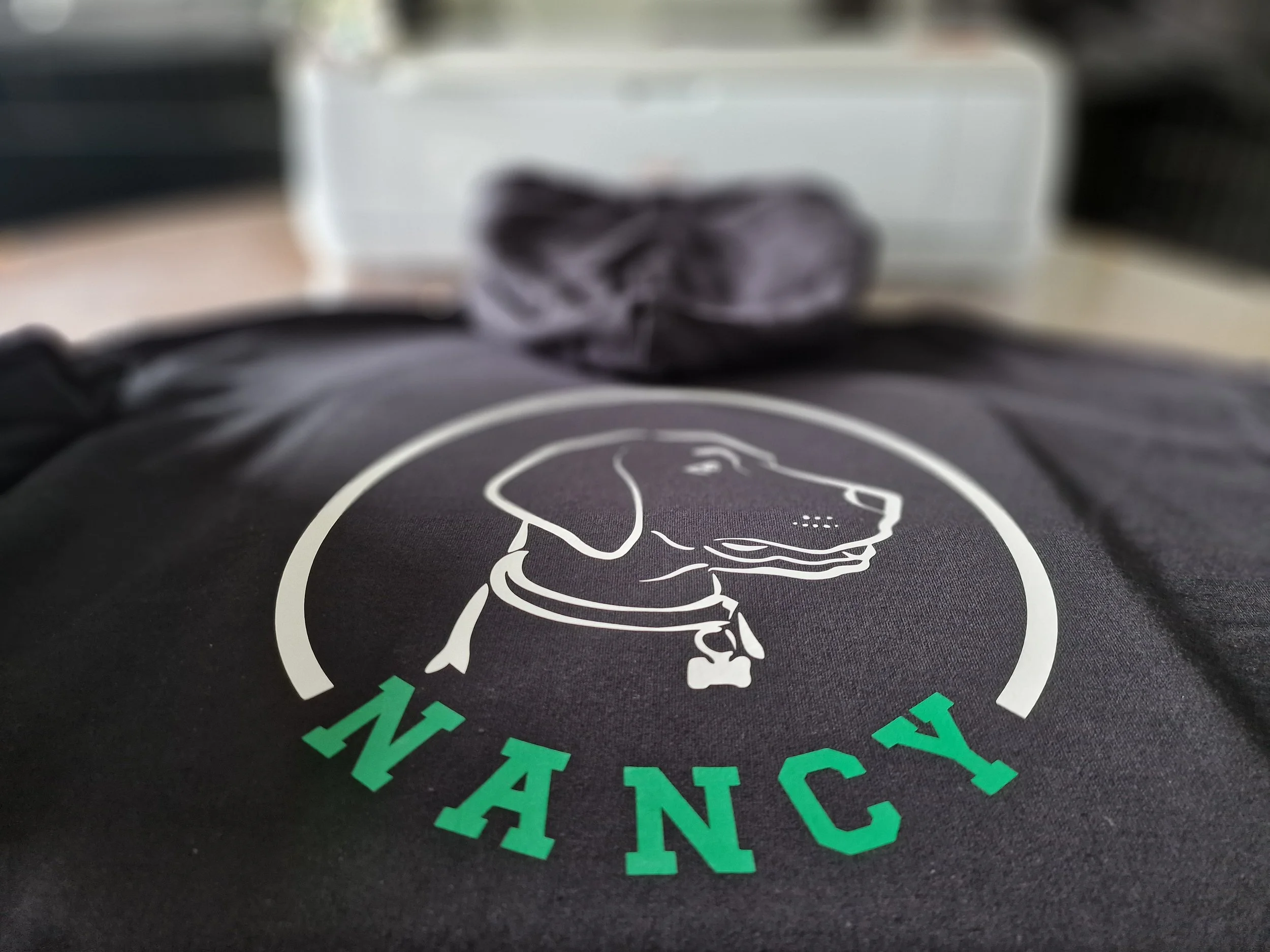 Close-up of a black personalised hoodie with a white illustration of a dog surrounded by green text.