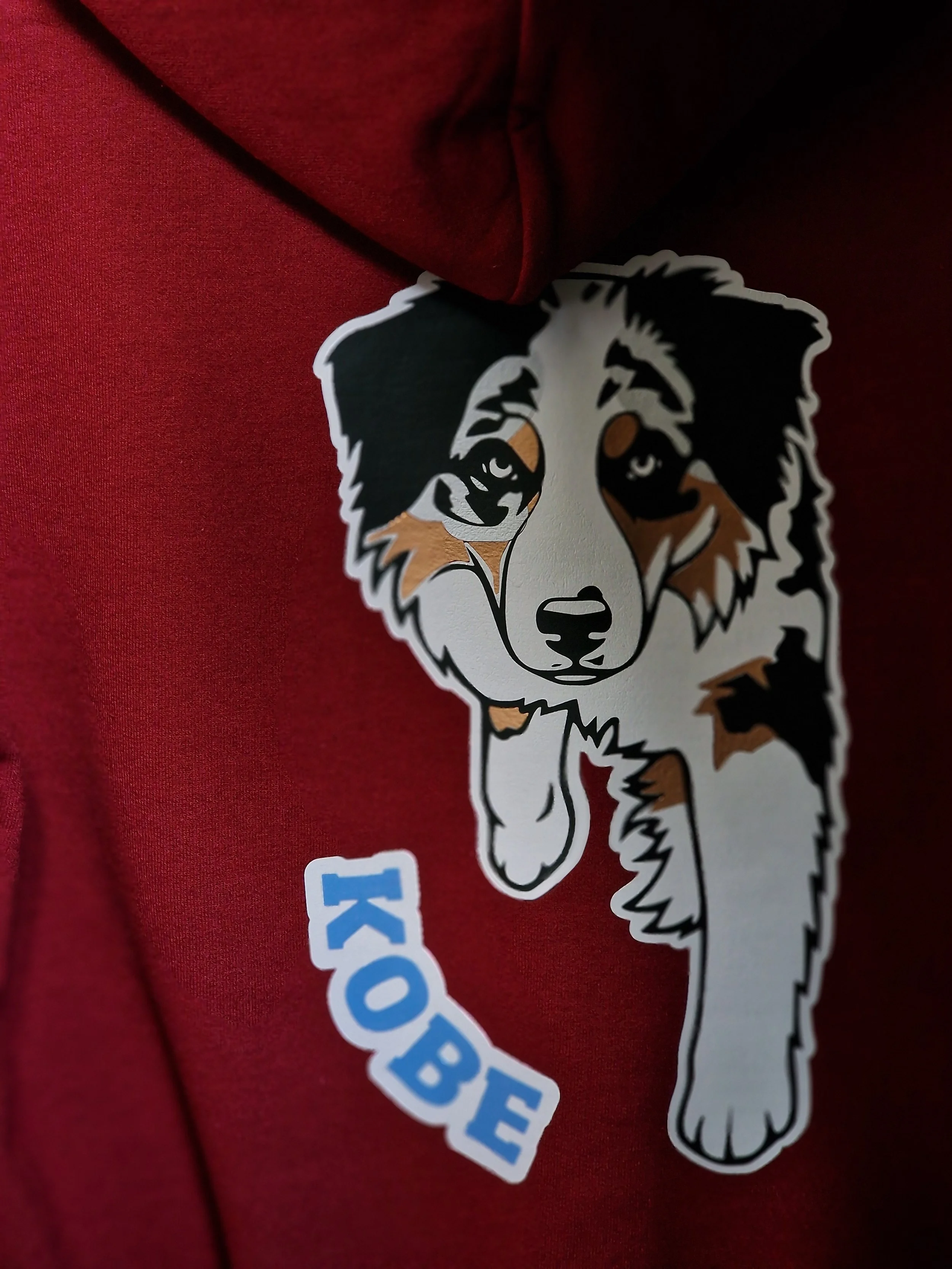 A sticker of a cartoon dog with black, white, and brown fur on a red fabric background.