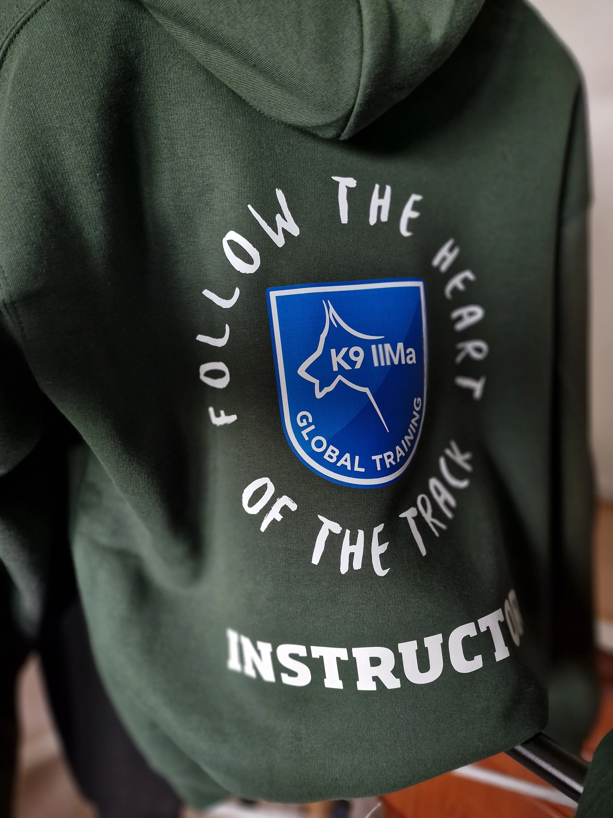 Close-up of a green jacket or vest with a logo that reads "K9 IIMa" and a dog paw graphic, part of a text that says "of the instruction."