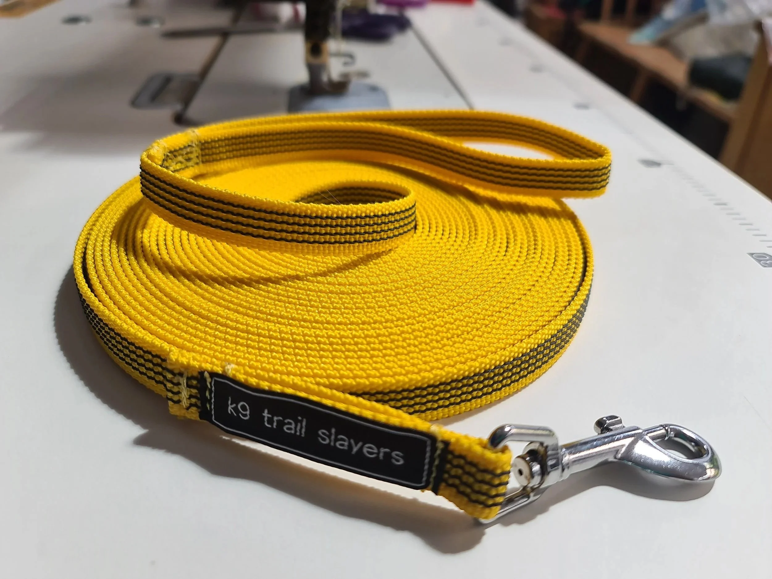 A coiled pink long line labeled 'k9 trail slayers' with a metal clip at one end, placed on a white surface with a measurement scale nearby.