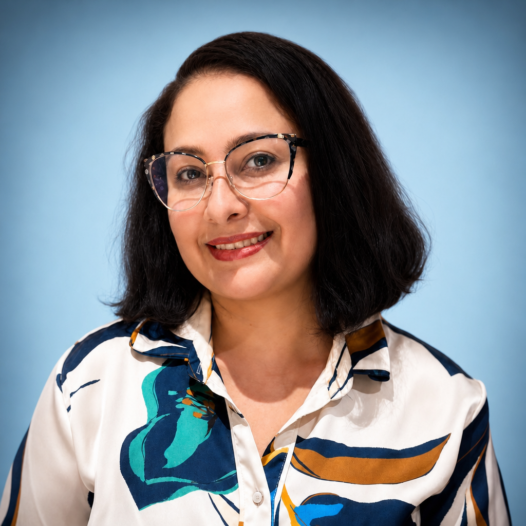 A woman with shoulder-length dark hair, wearing glasses and a patterned blouse, smiling against a blue background.