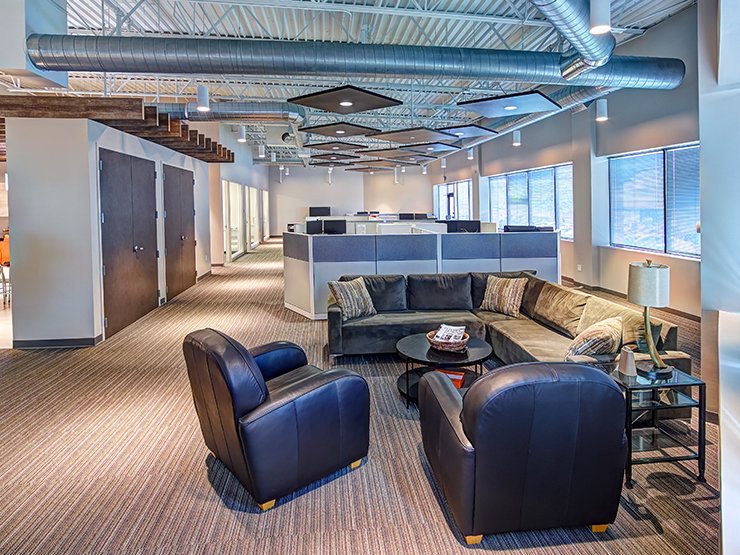 Modern office lounge with leather armchairs, sectional sofa, coffee table, and open workstations