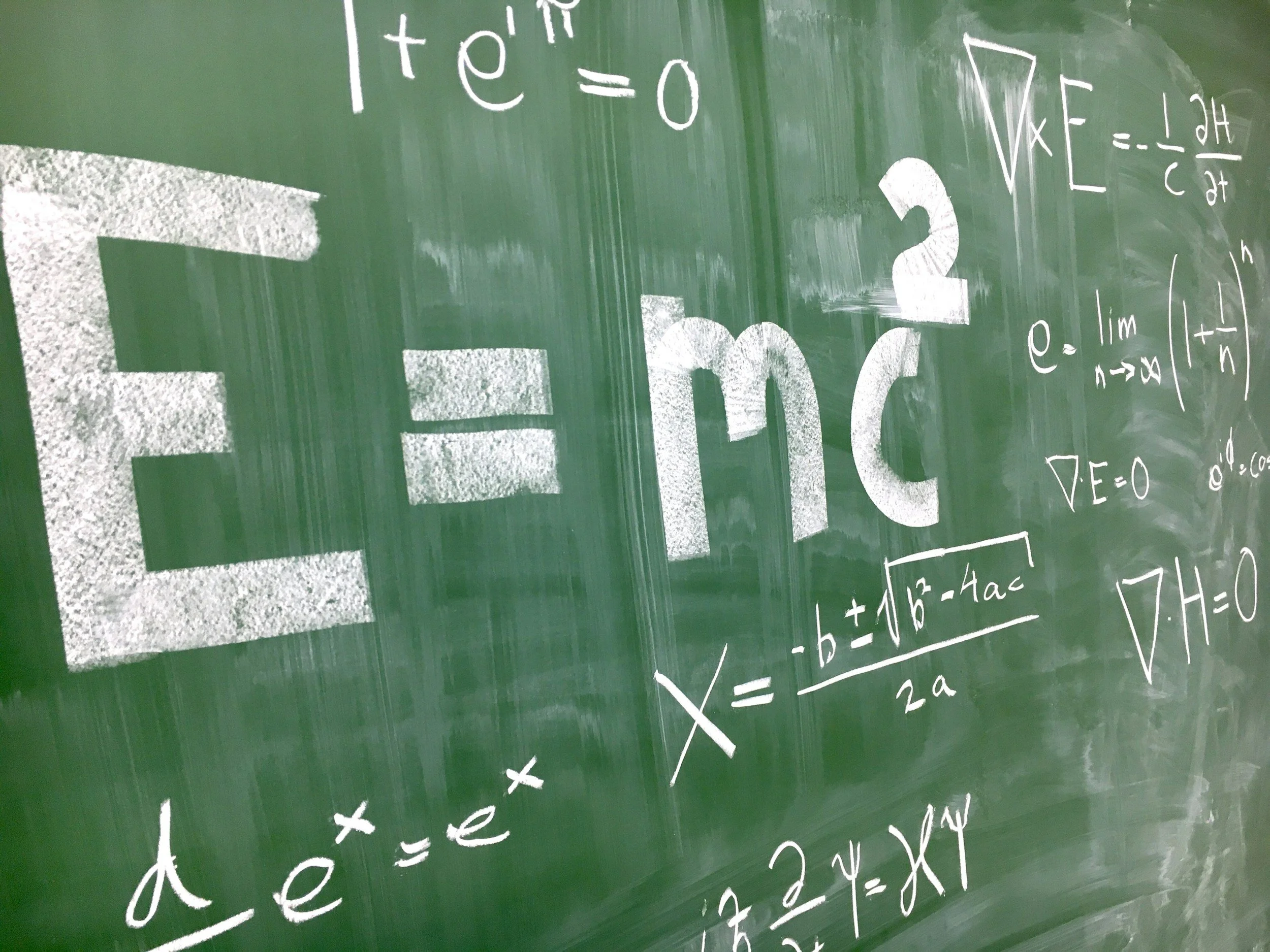 Green chalkboard with various math formulas and equations written in white chalk, including algebra and calculus.