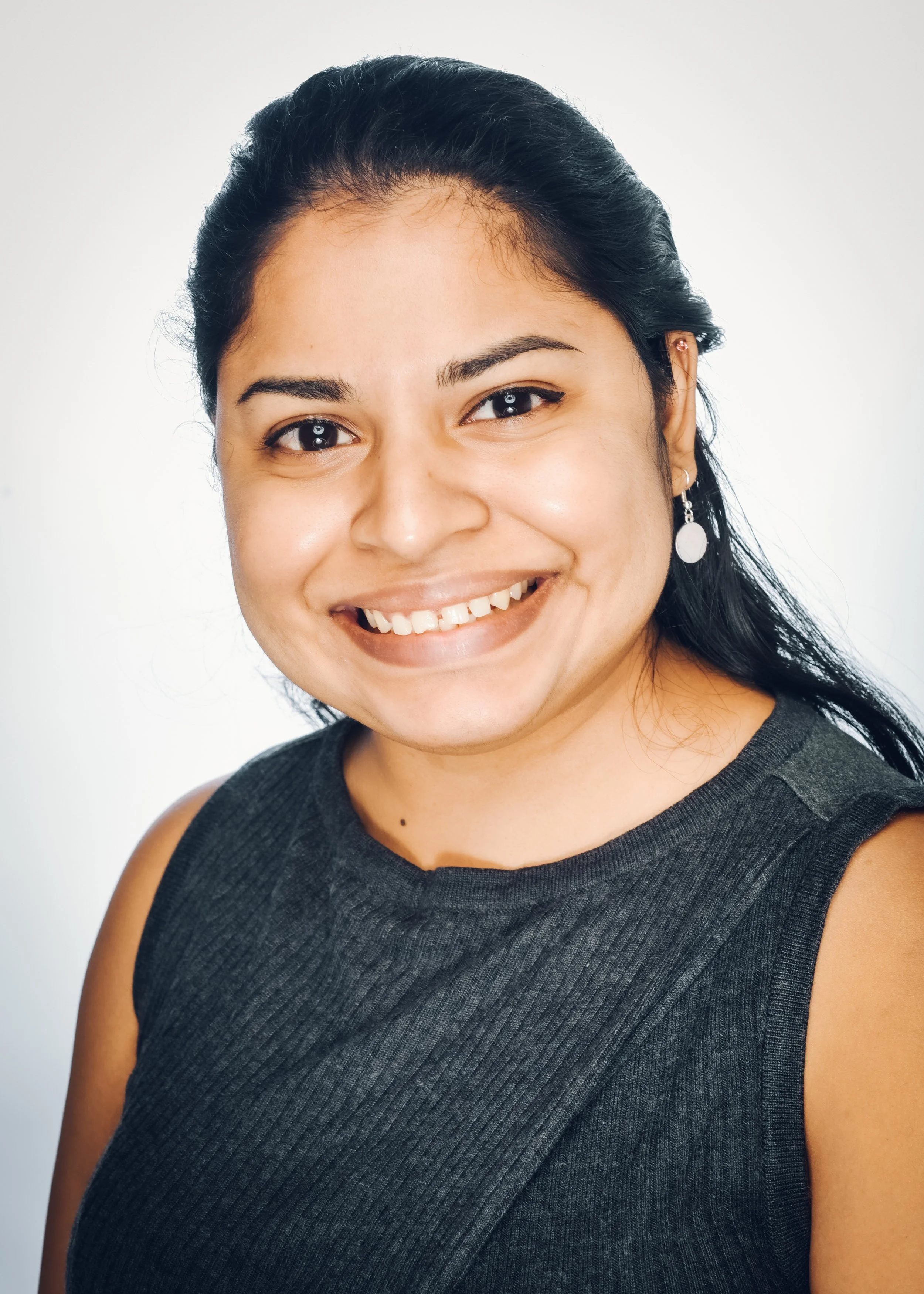 Close-up of Varuna Deopersad with dark hair and earrings, wearing a sleeveless black top, against a plain white background.